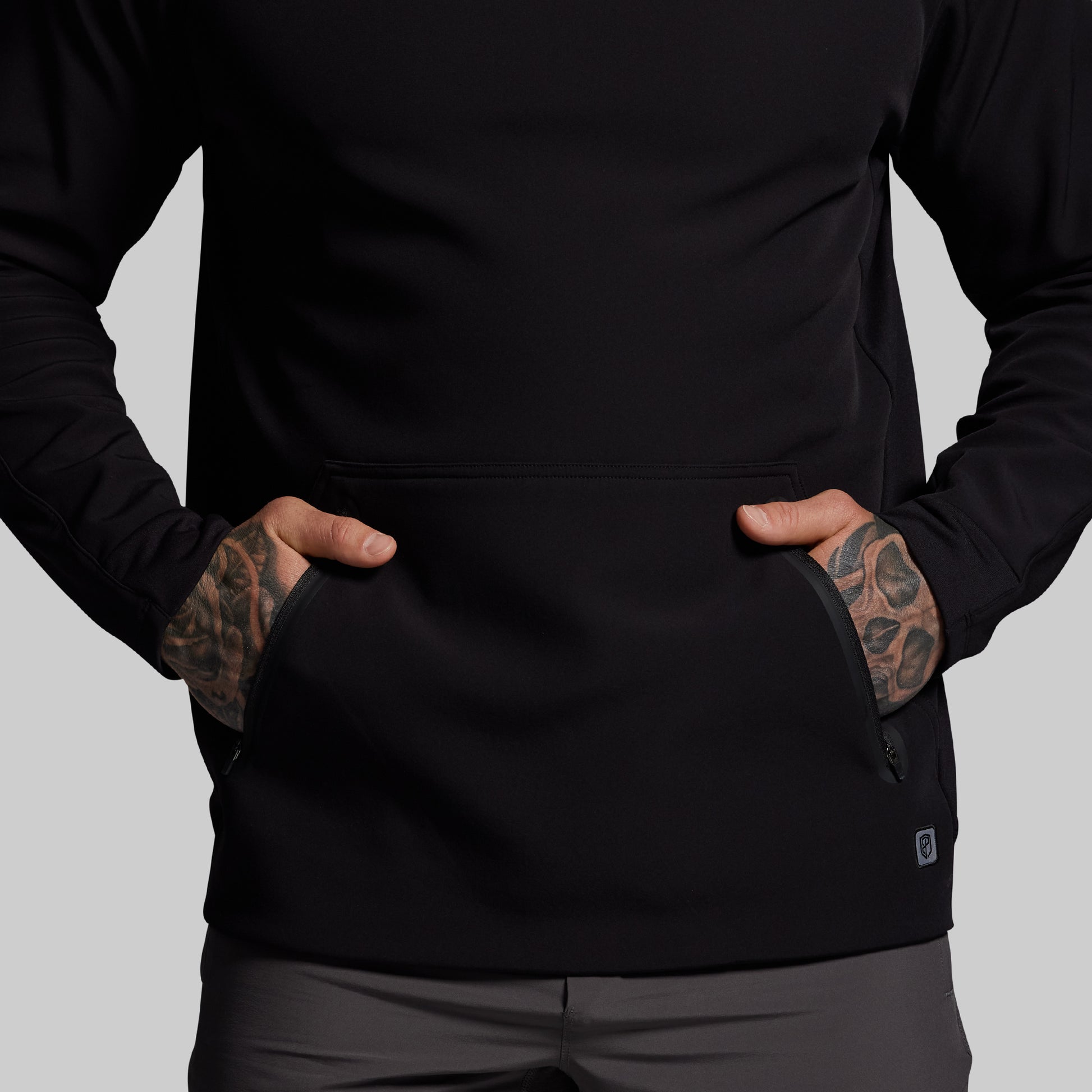 Person wearing a black jacket with tattoos on arms against a gray background