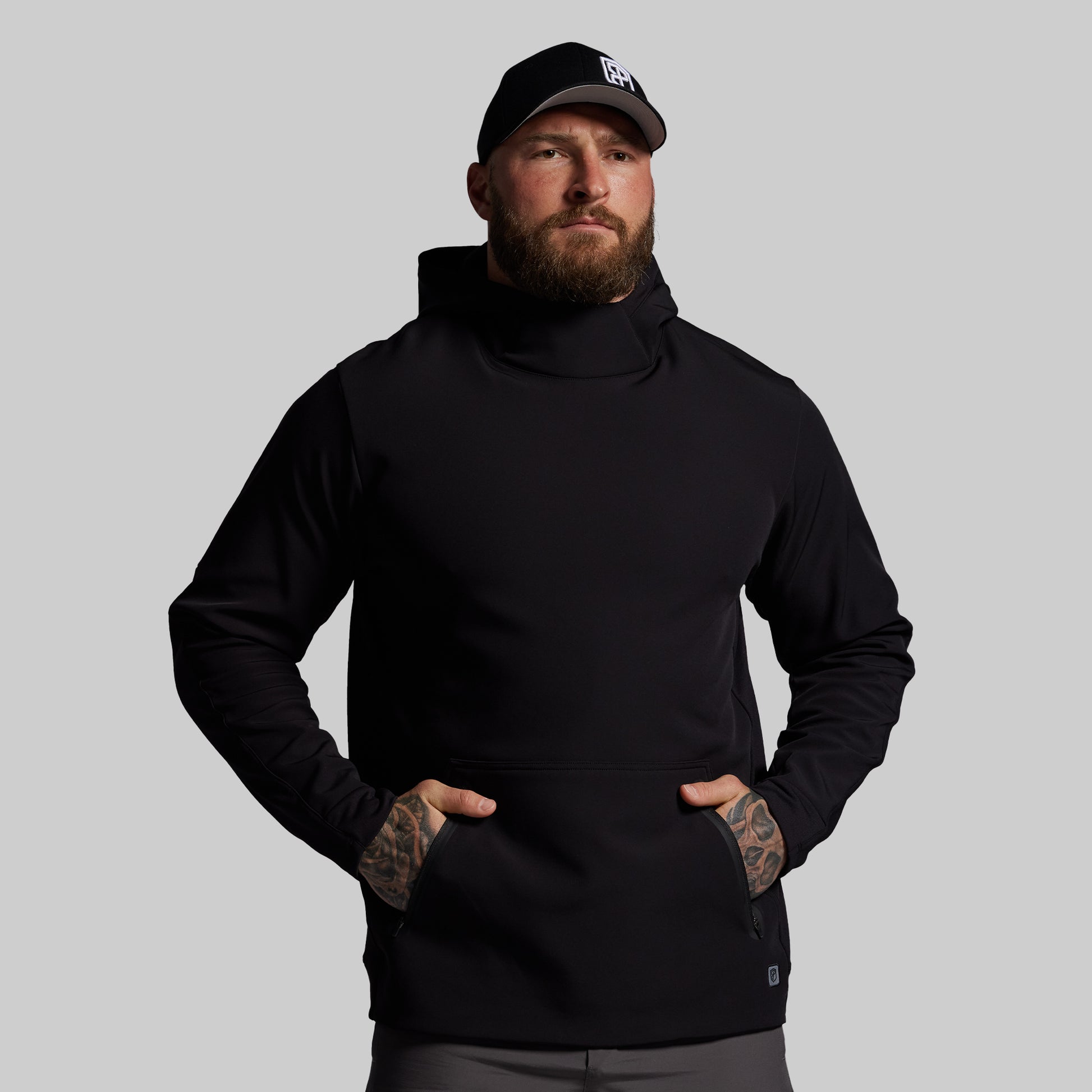 Man wearing a black hoodie and cap on a gray background