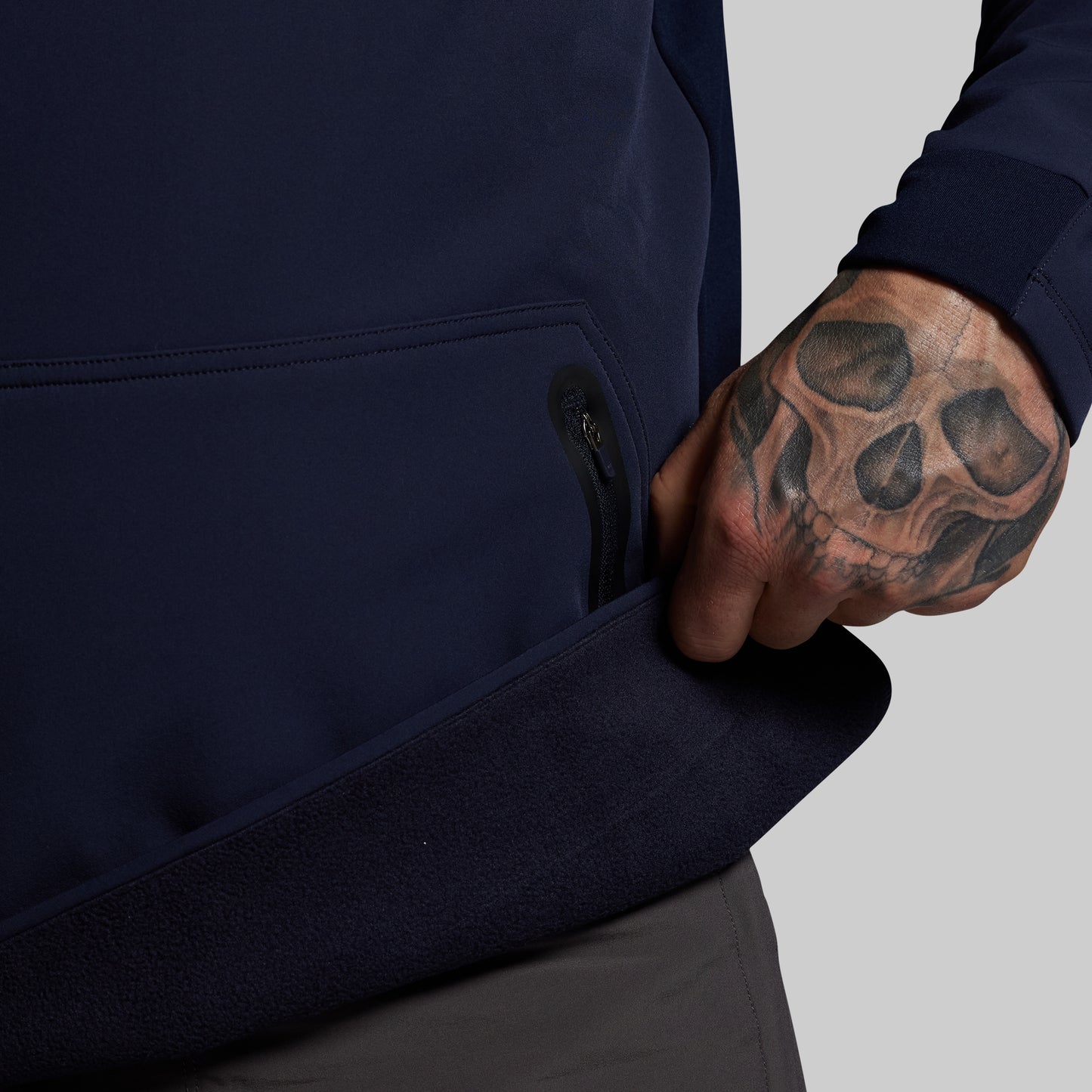 Person wearing a navy blue jacket with a tattooed hand on a gray background
