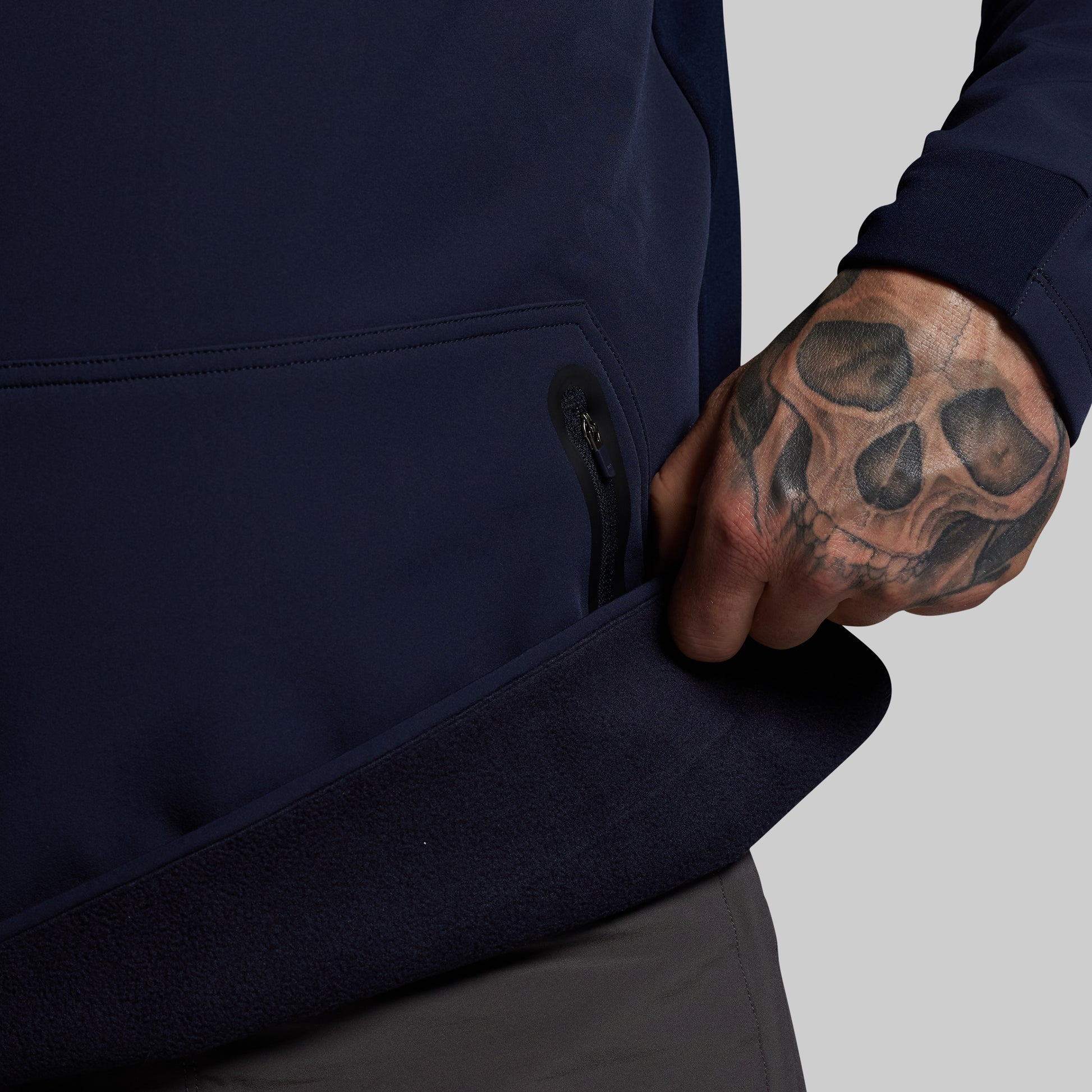 Person wearing a navy blue jacket with a tattooed hand on a gray background
