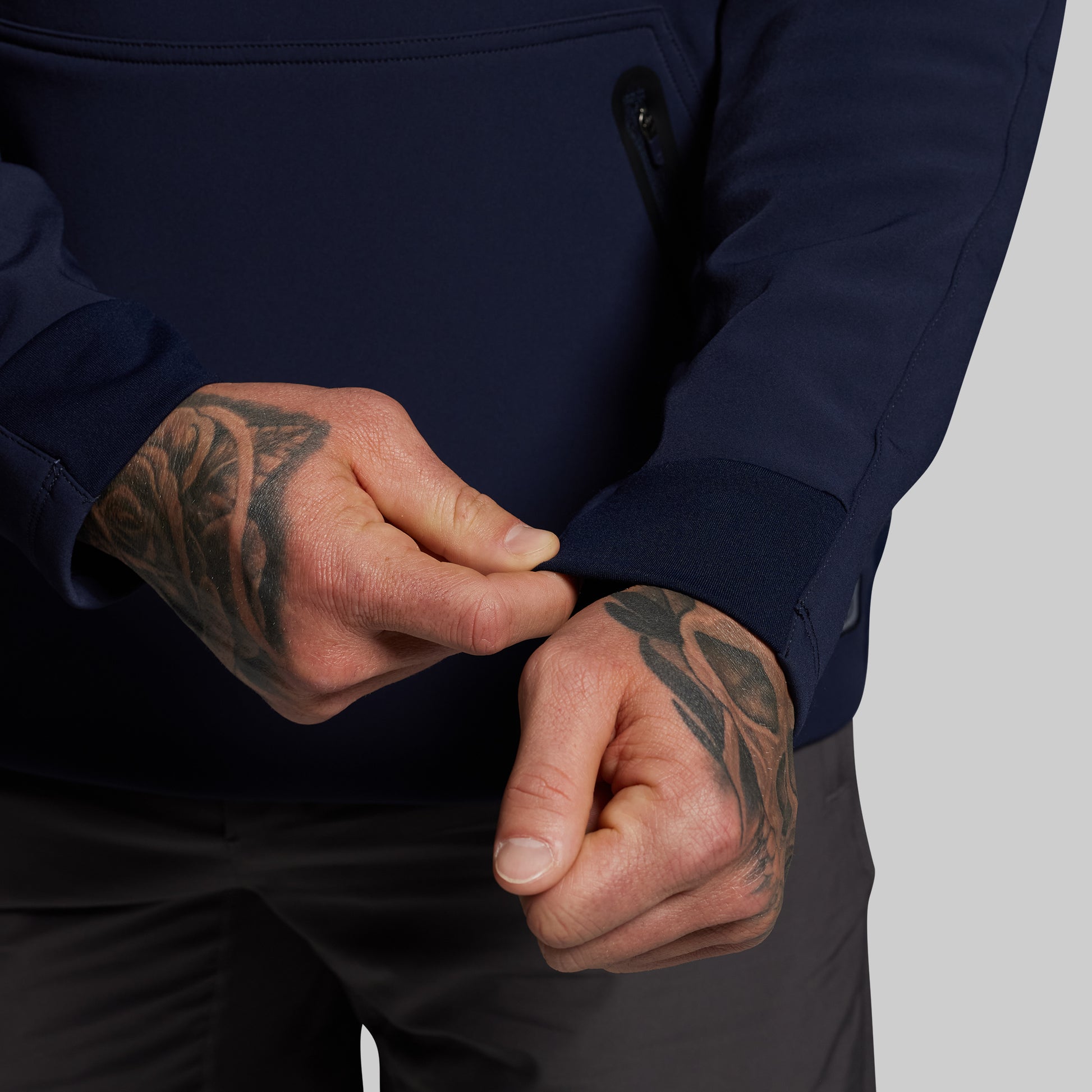 Person wearing a navy jacket with tattooed hands on a gray background
