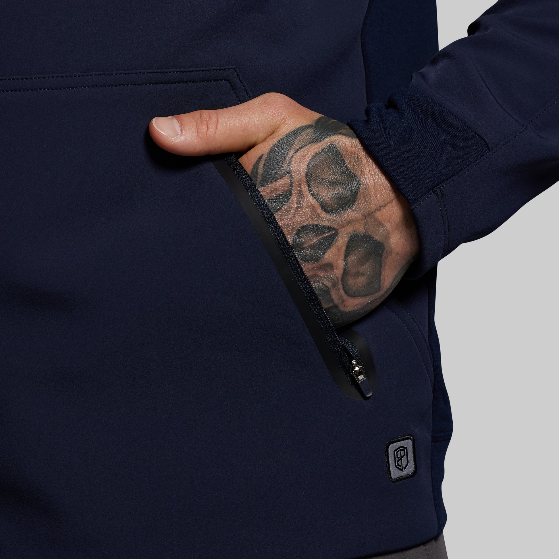 Navy blue hoodie with a hand reaching into a pocket, showing a tattooed arm.
