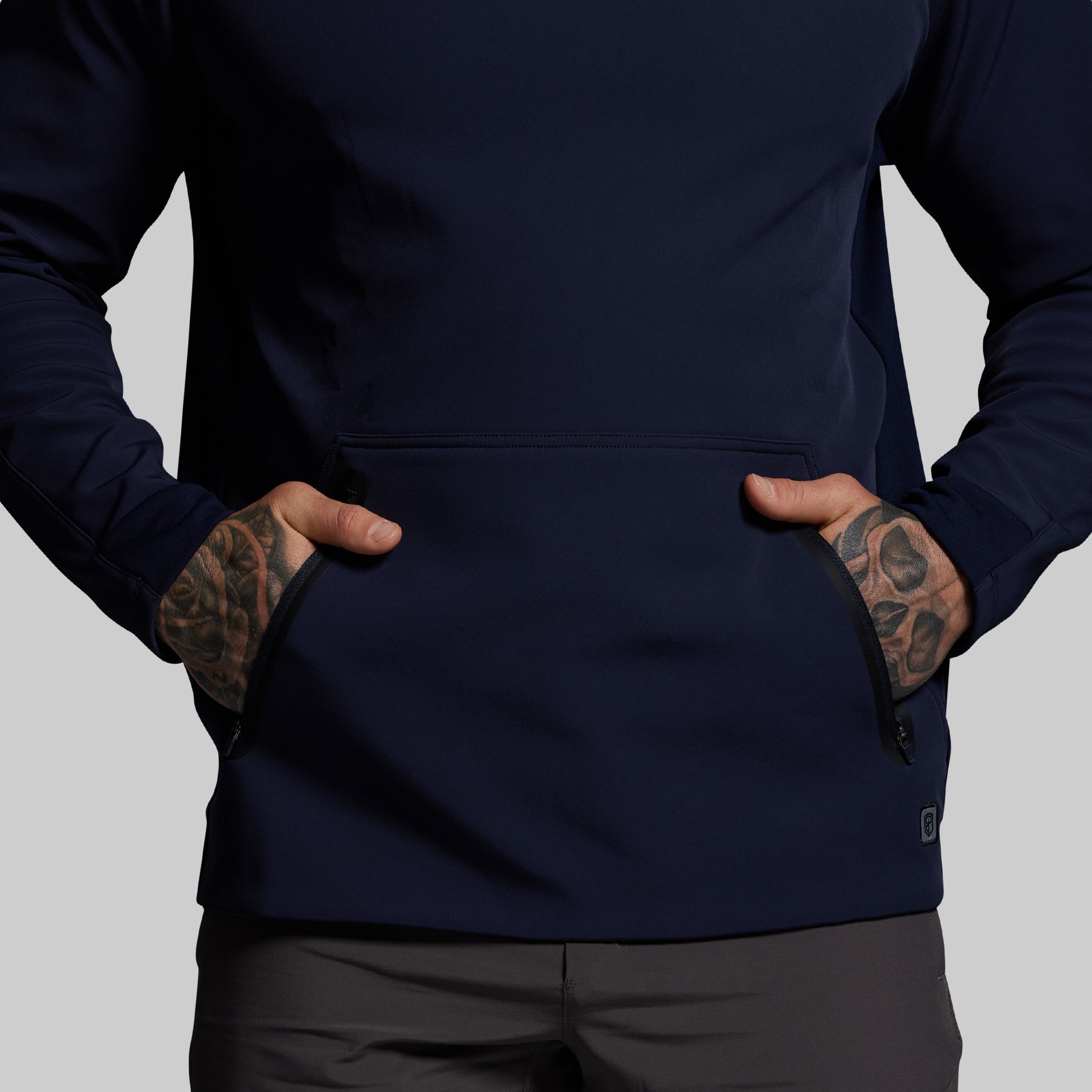 Person wearing a navy blue jacket with tattoos on arms against a gray background