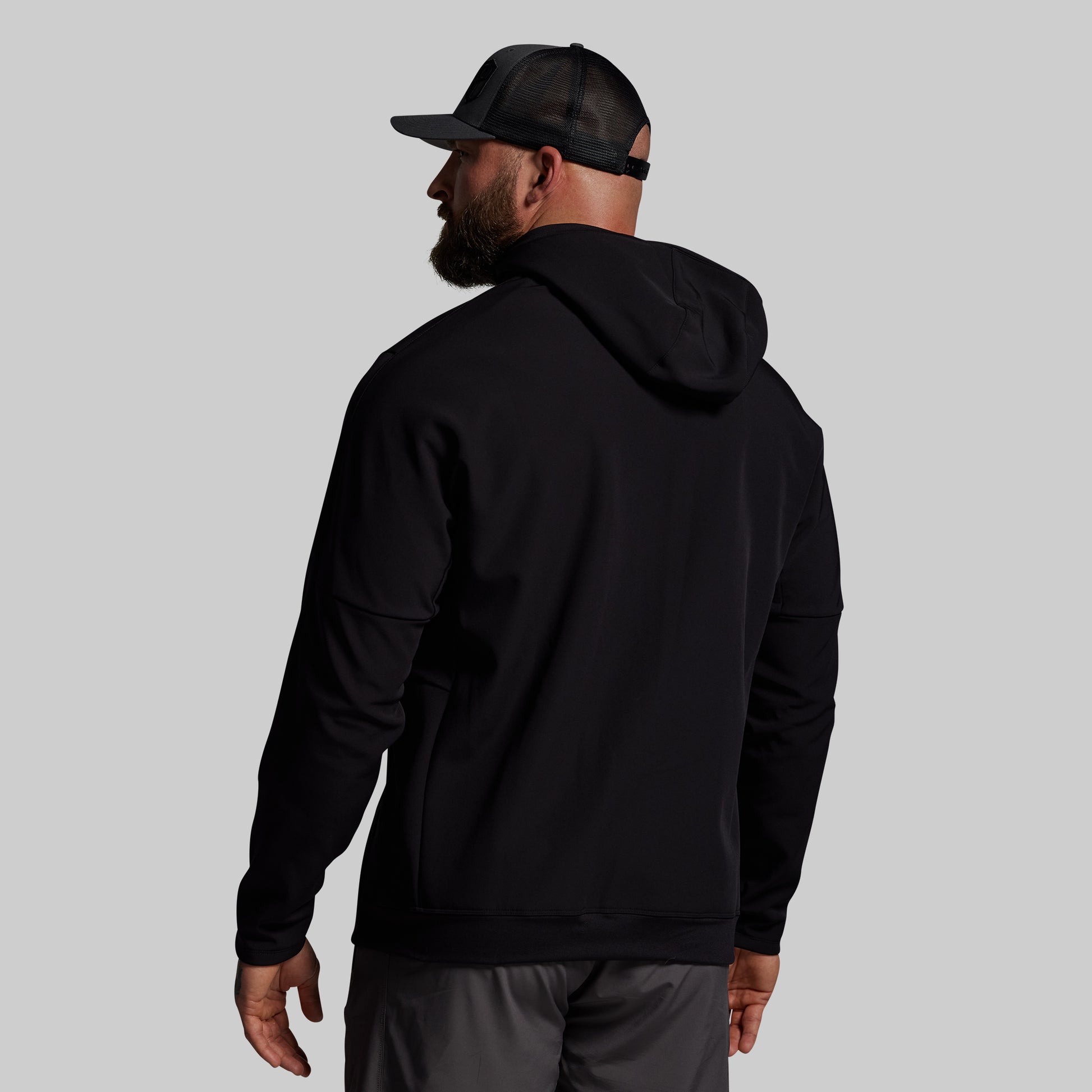 Man wearing a black hoodie and cap from behind on a light gray background