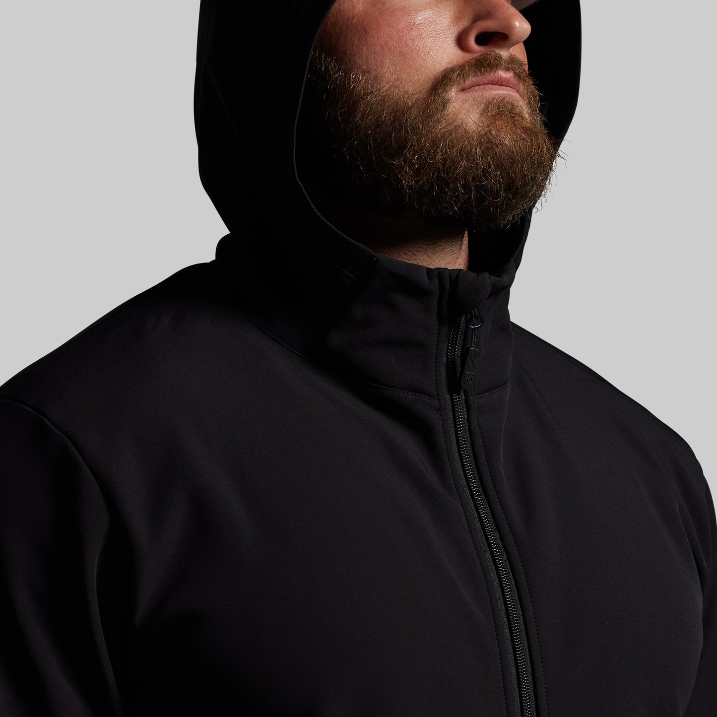 Man wearing a black full zip with a hood against a gray background
