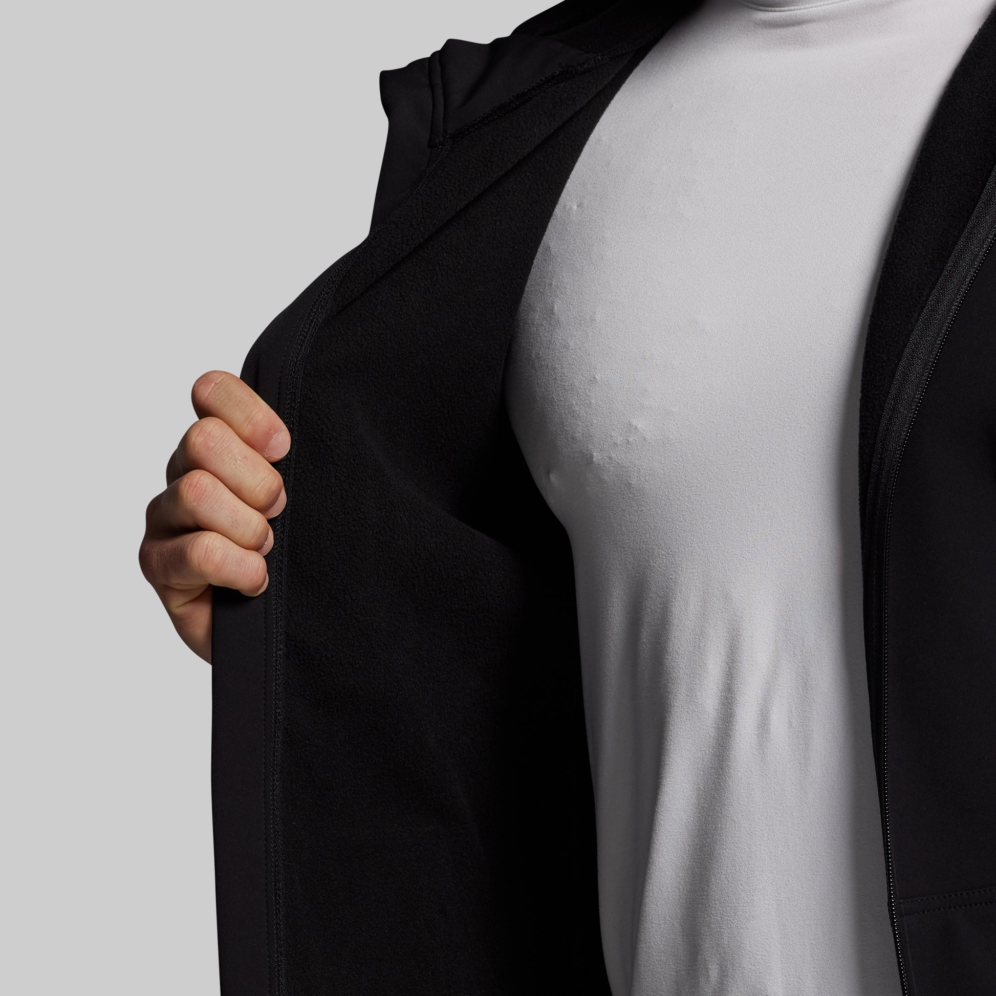 Person wearing a black full zip hoodie over a white shirt on a plain background