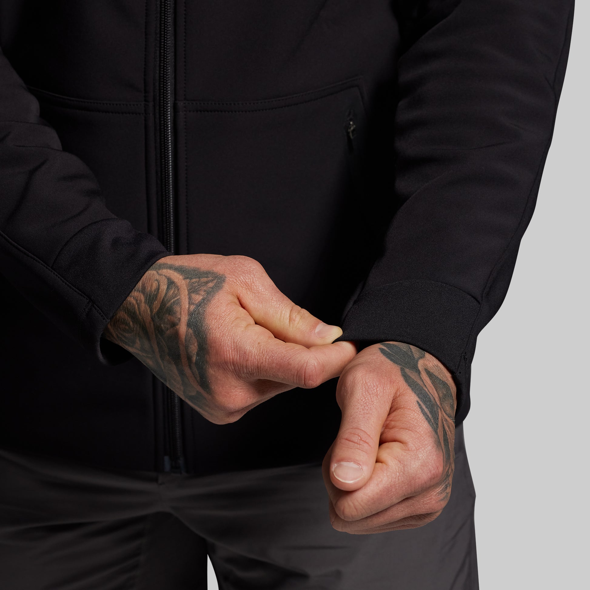 Person wearing a black hoodie with tattooed hands on a gray background