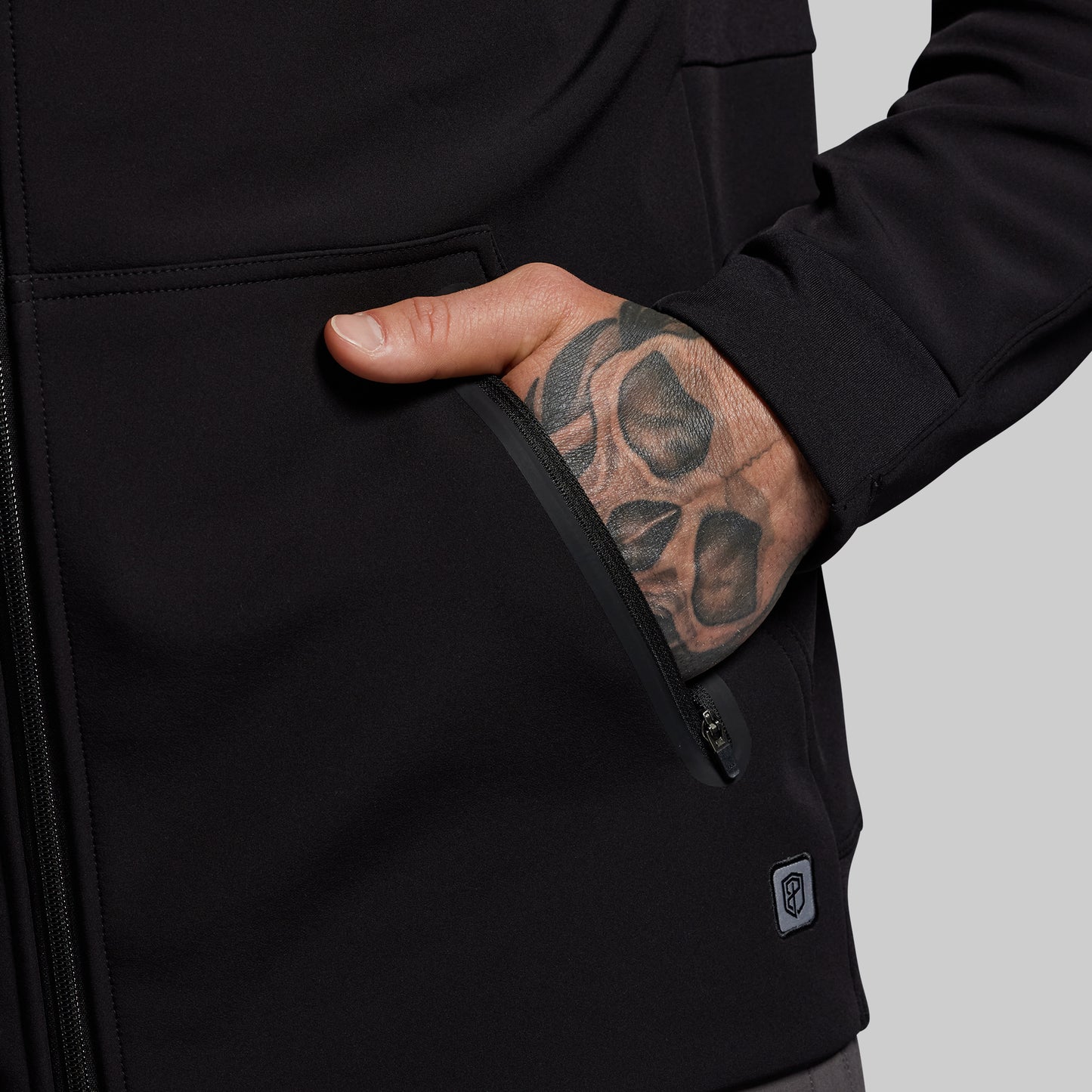 Person wearing a black hoodie with a tattooed hand on a gray background