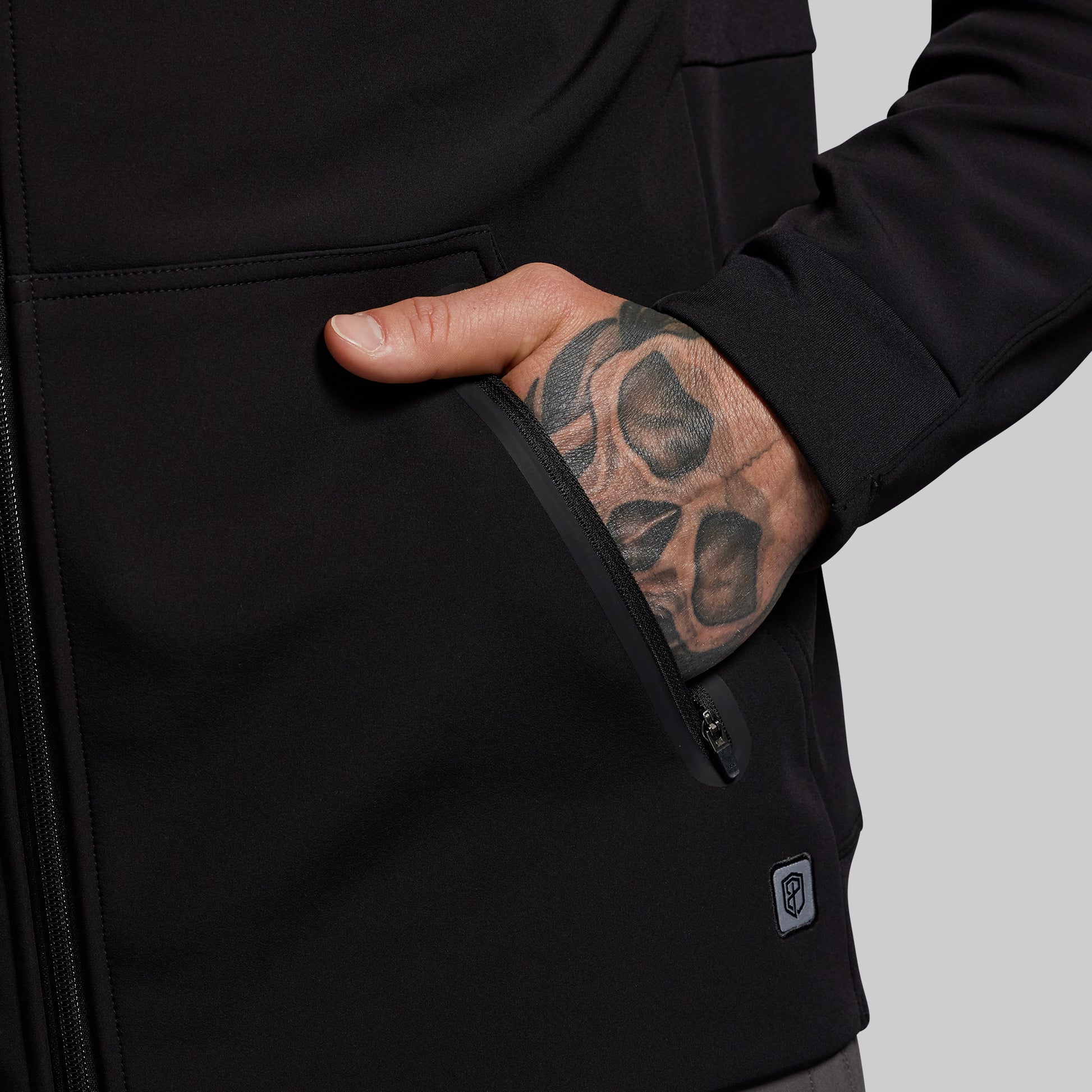 Person wearing a black hoodie with a tattooed hand on a gray background