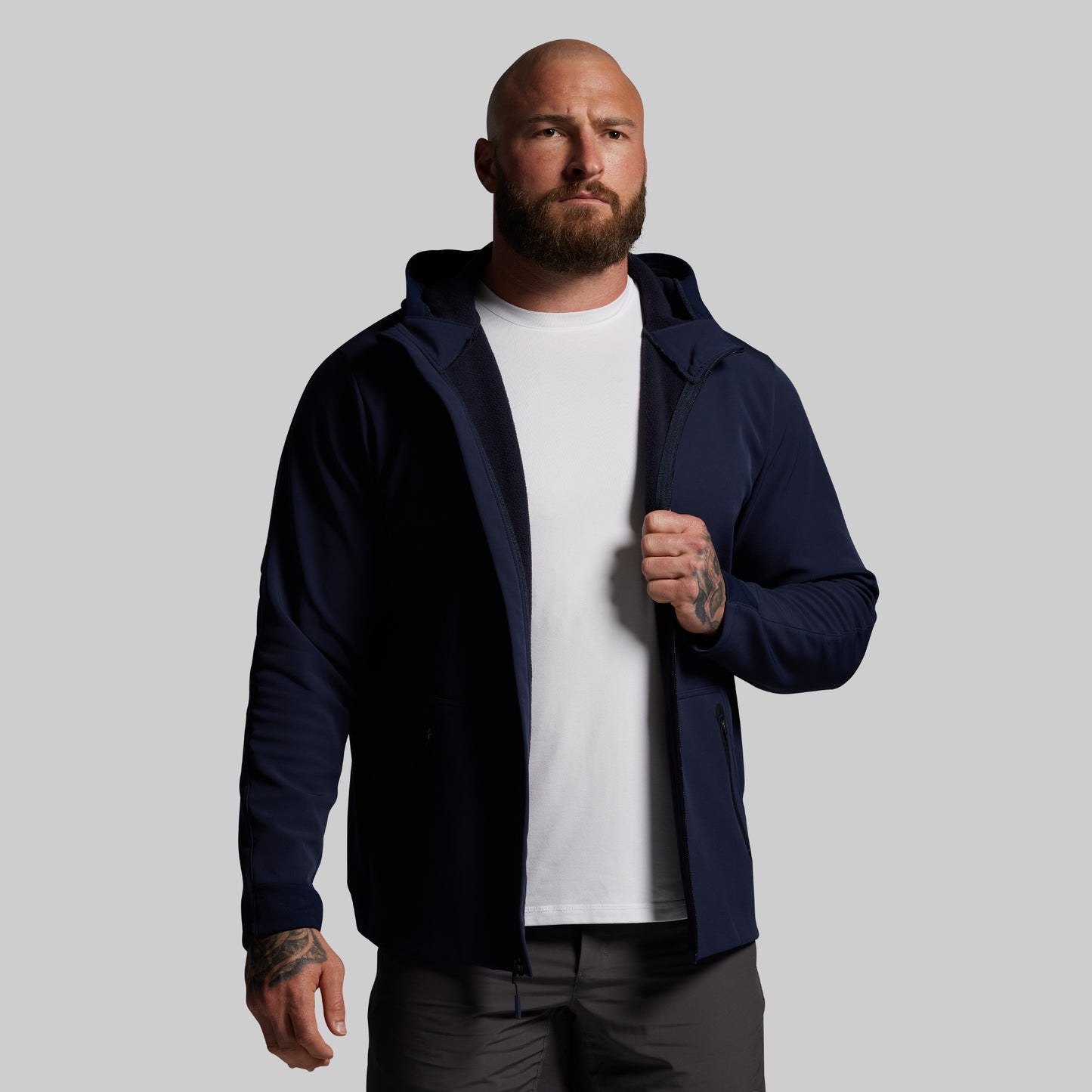 Man wearing a navy blue full zip hoodie over a white shirt on a gray background