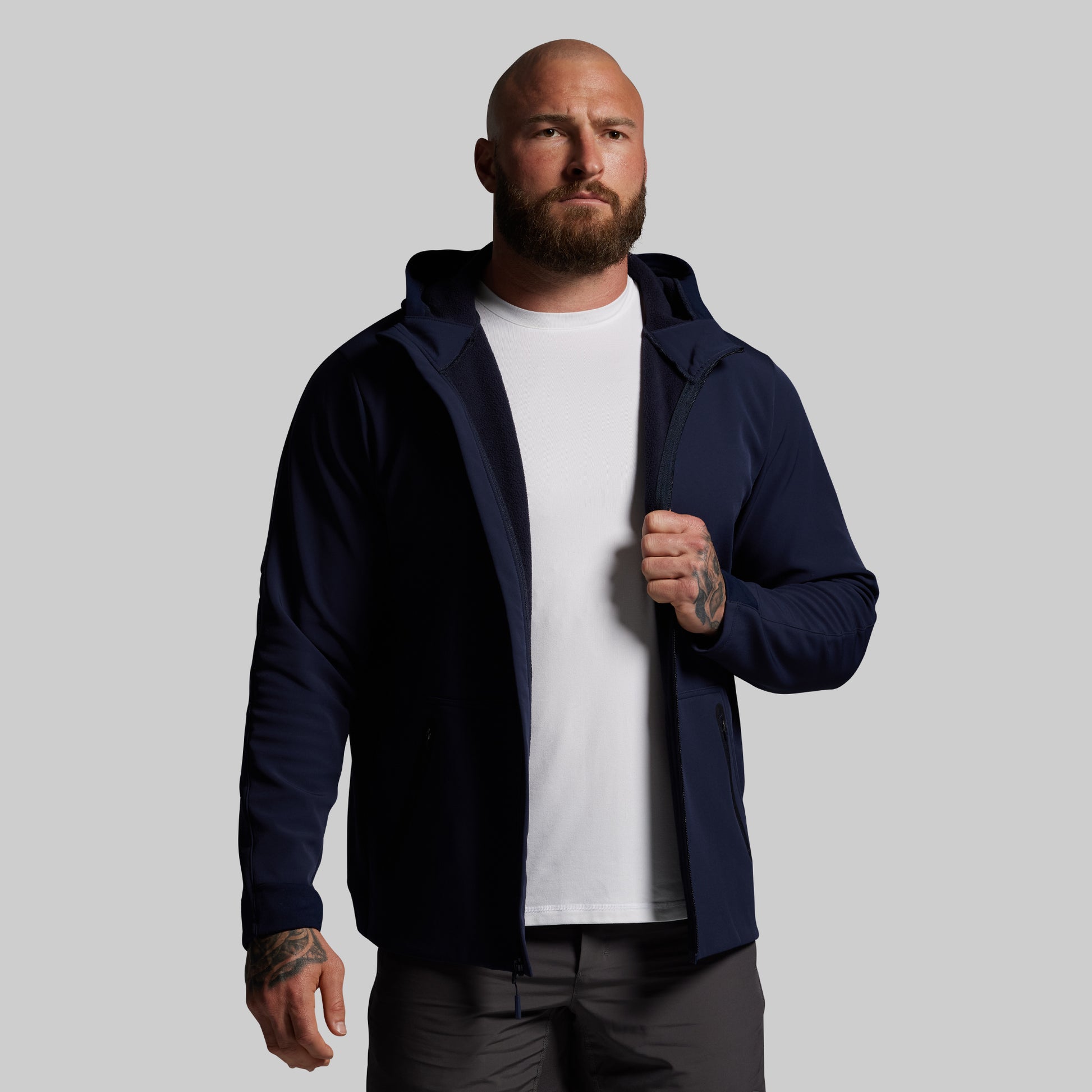 Man wearing a navy blue full zip hoodie over a white shirt on a gray background
