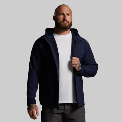 Man wearing a navy blue full zip hoodie over a white shirt on a gray background