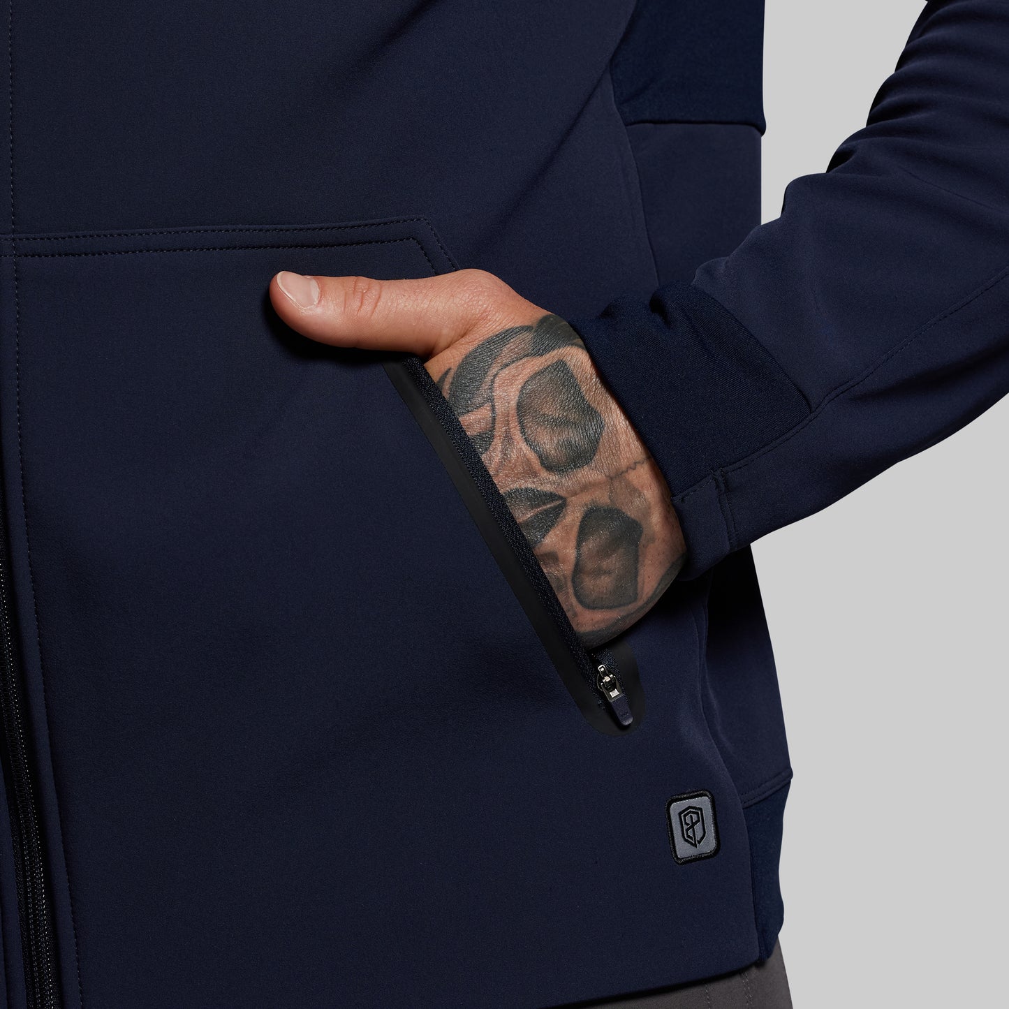 Navy blue jacket with a hand reaching into a pocket, showing a tattooed arm.