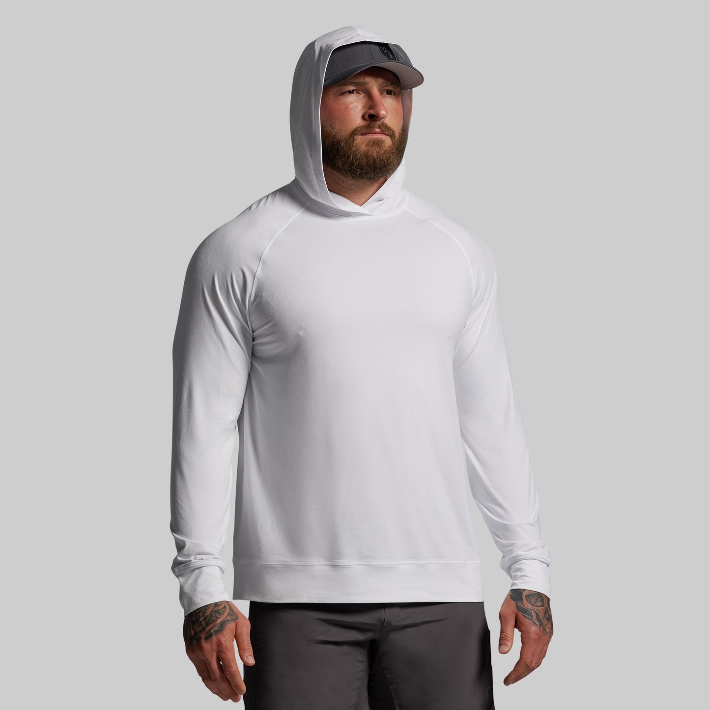 Man wearing a white hoodie and black cap against a gray background