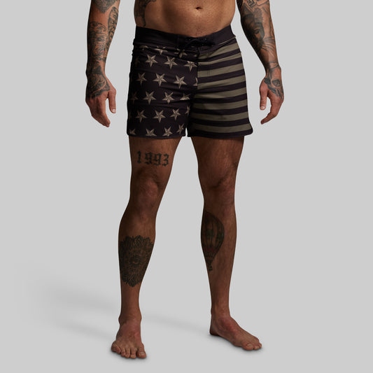 Person wearing black swim shorts with star and stripe pattern on a gray background