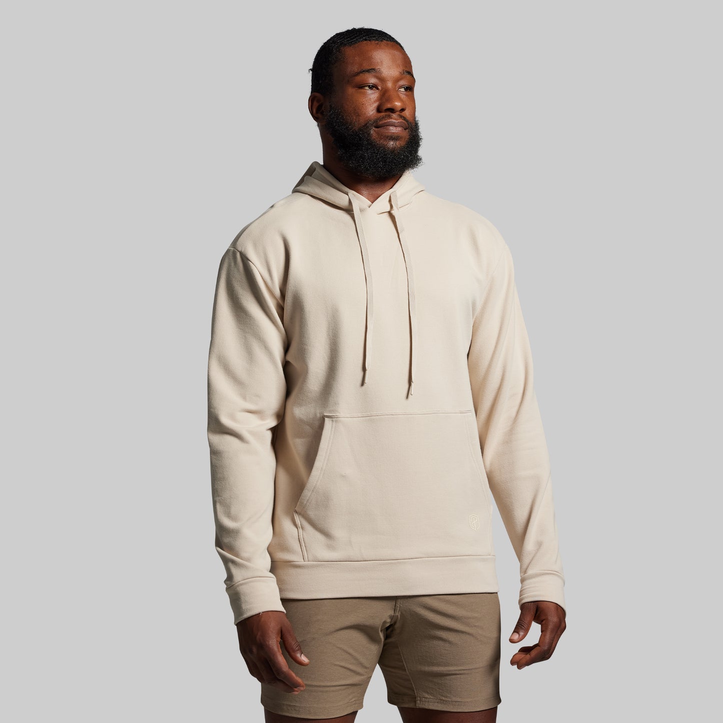 Man wearing a beige hoodie and shorts on a gray background
