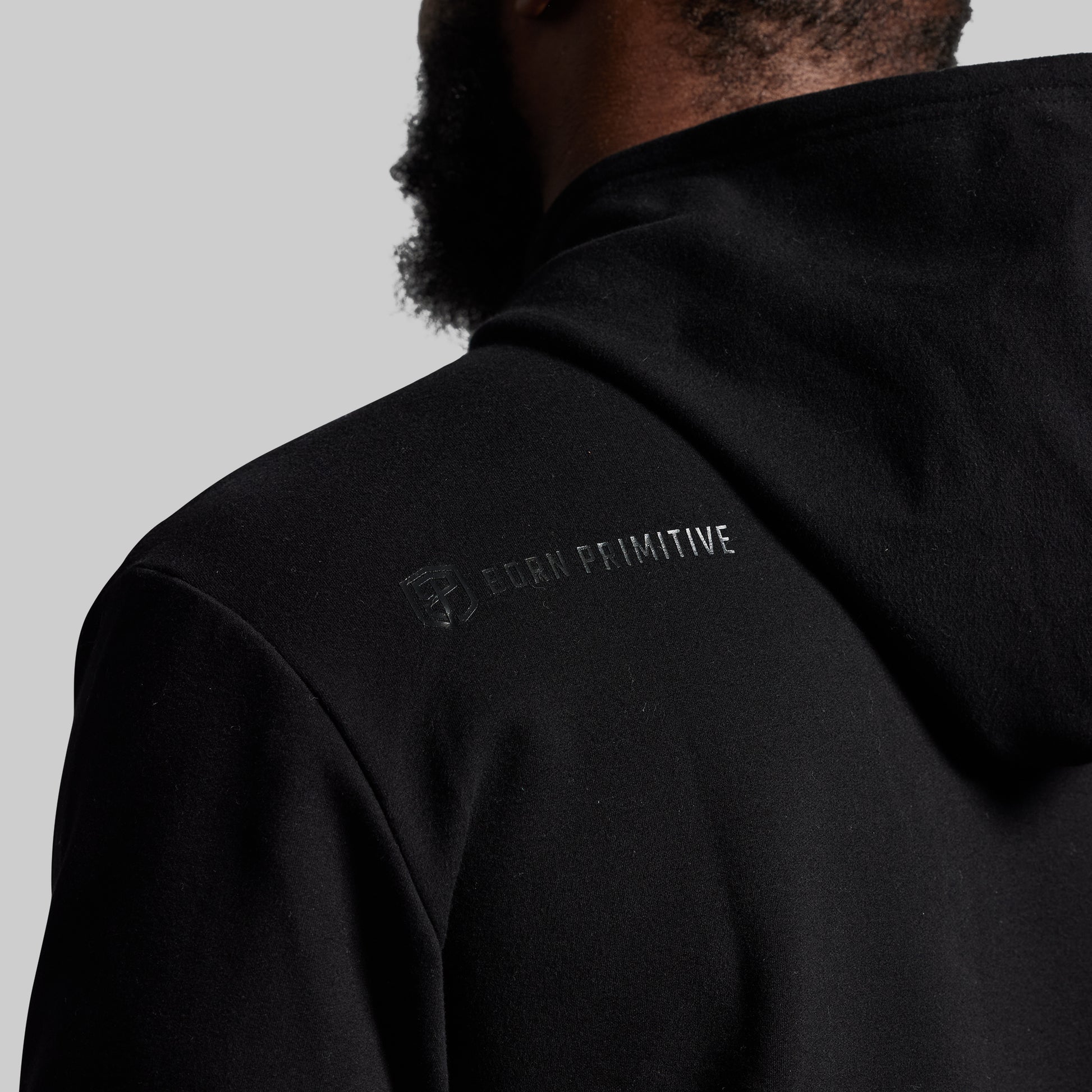 Person wearing a black hoodie with a brand logo on the back against a gray background