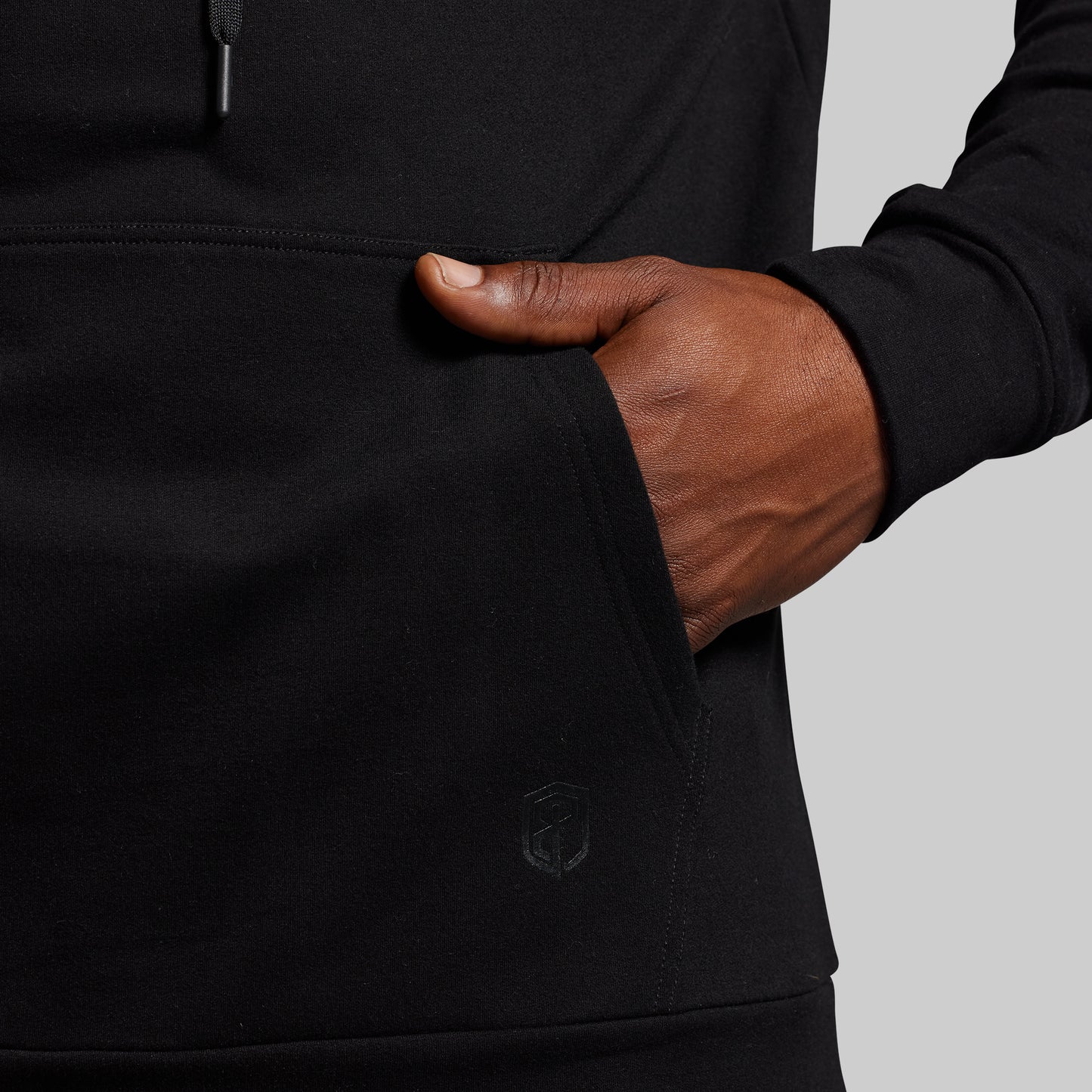 Hand inserting into a black hoodie pocket against a gray background