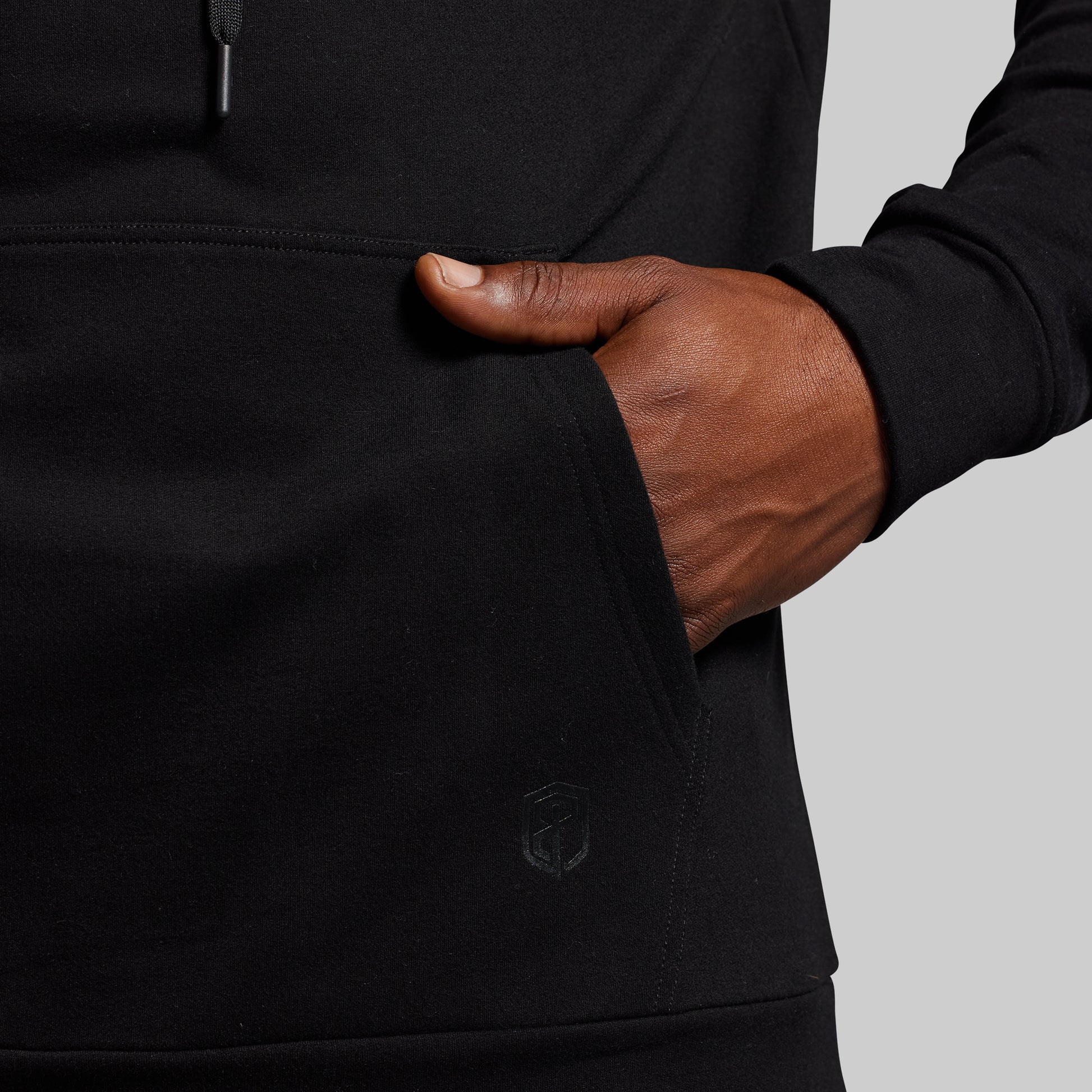Hand inserting into a black hoodie pocket against a gray background
