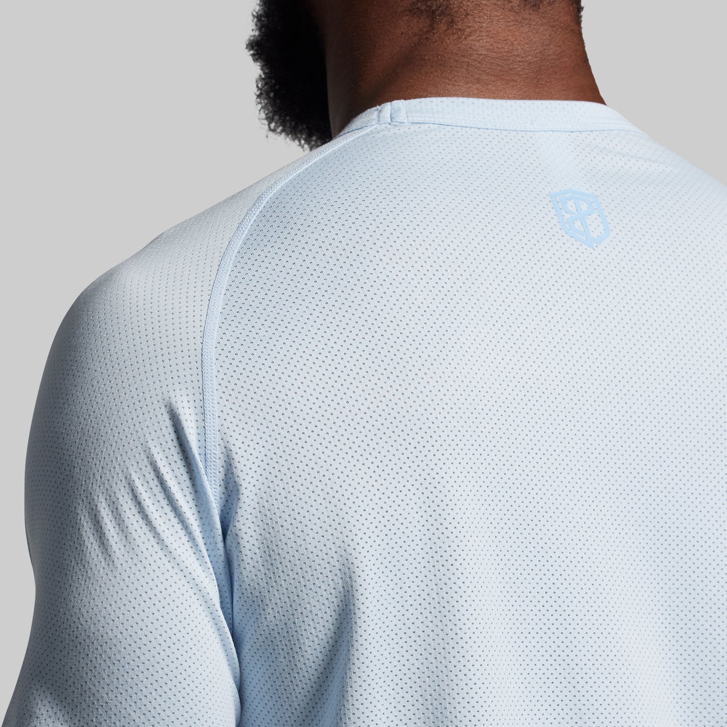 Close-up of a man's back wearing a light blue, short-sleeved, mesh athletic shirt.