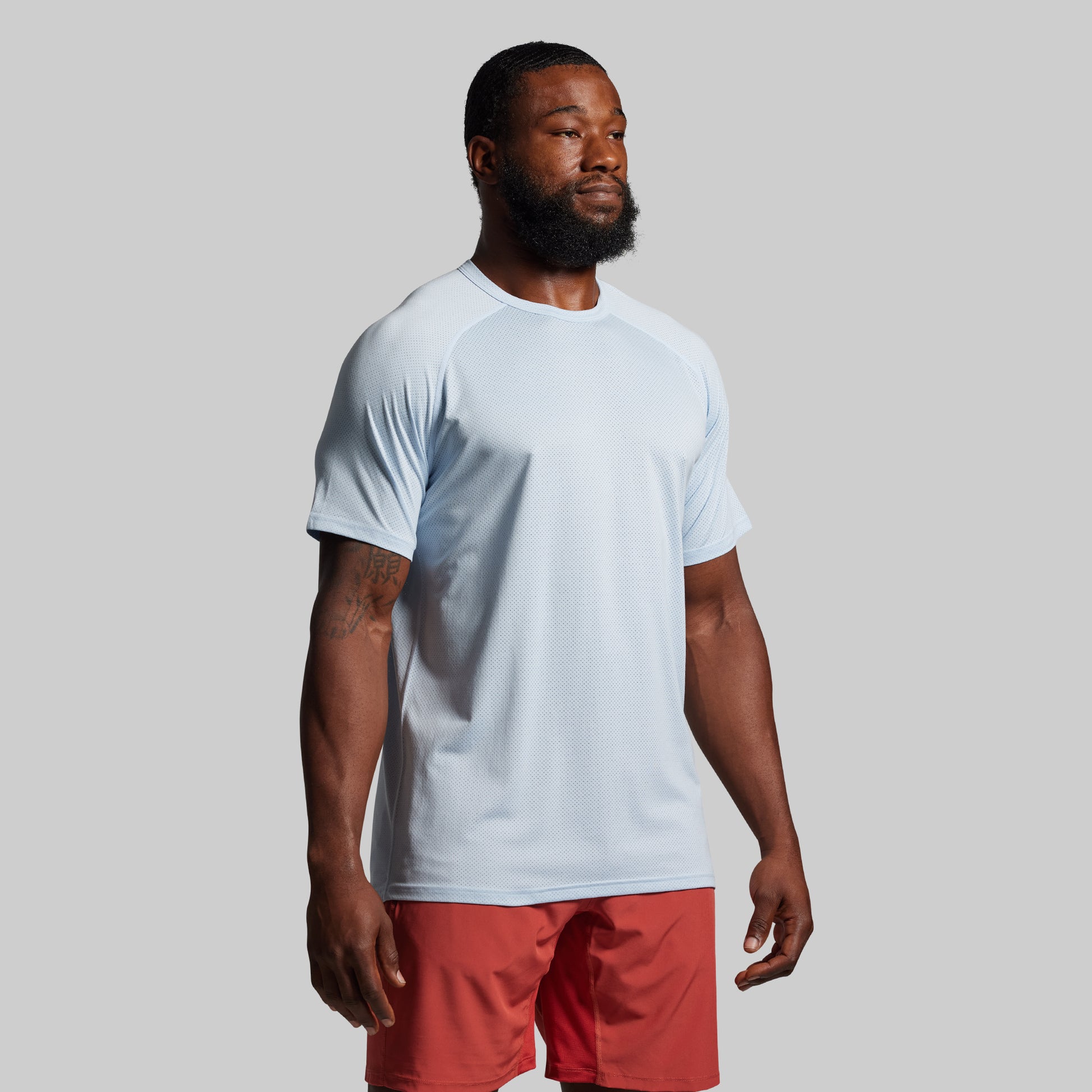 Man wearing a light blue t-shirt and red shorts on a gray background