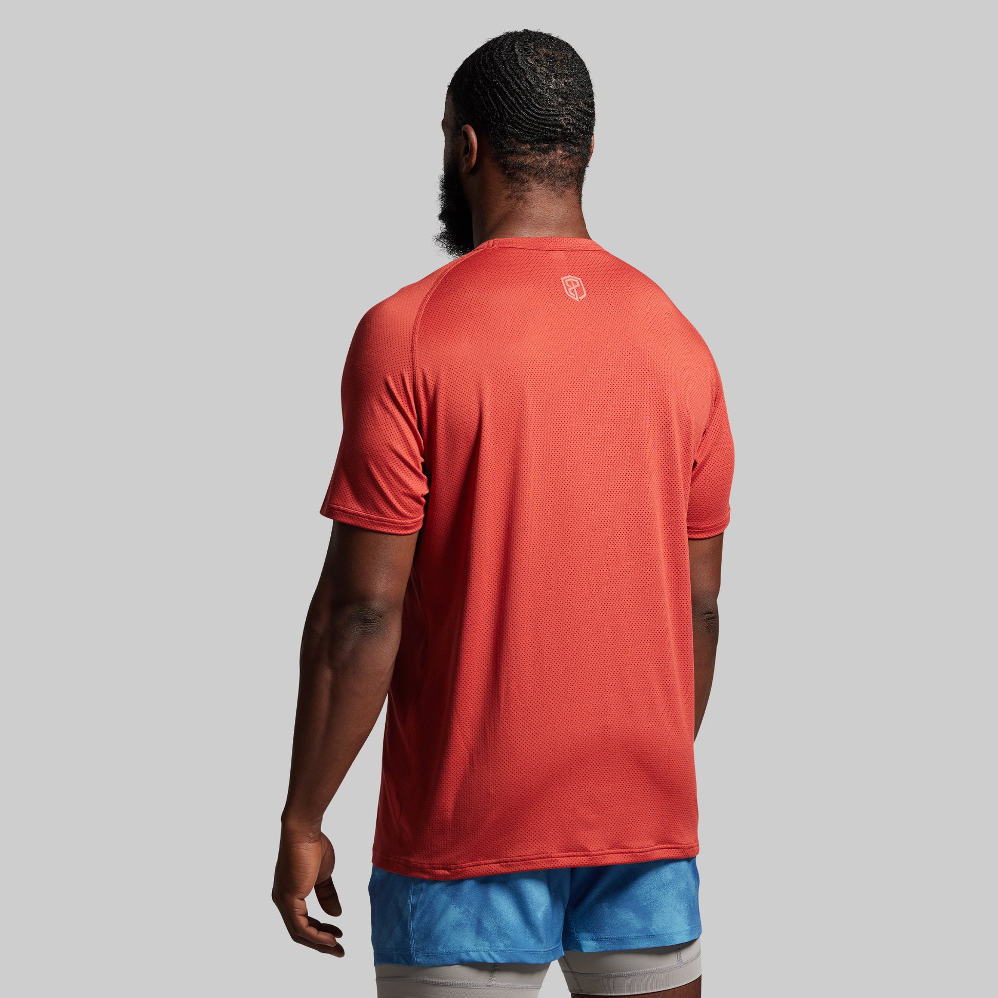 Person wearing an orange sports shirt and blue shorts against a gray background.