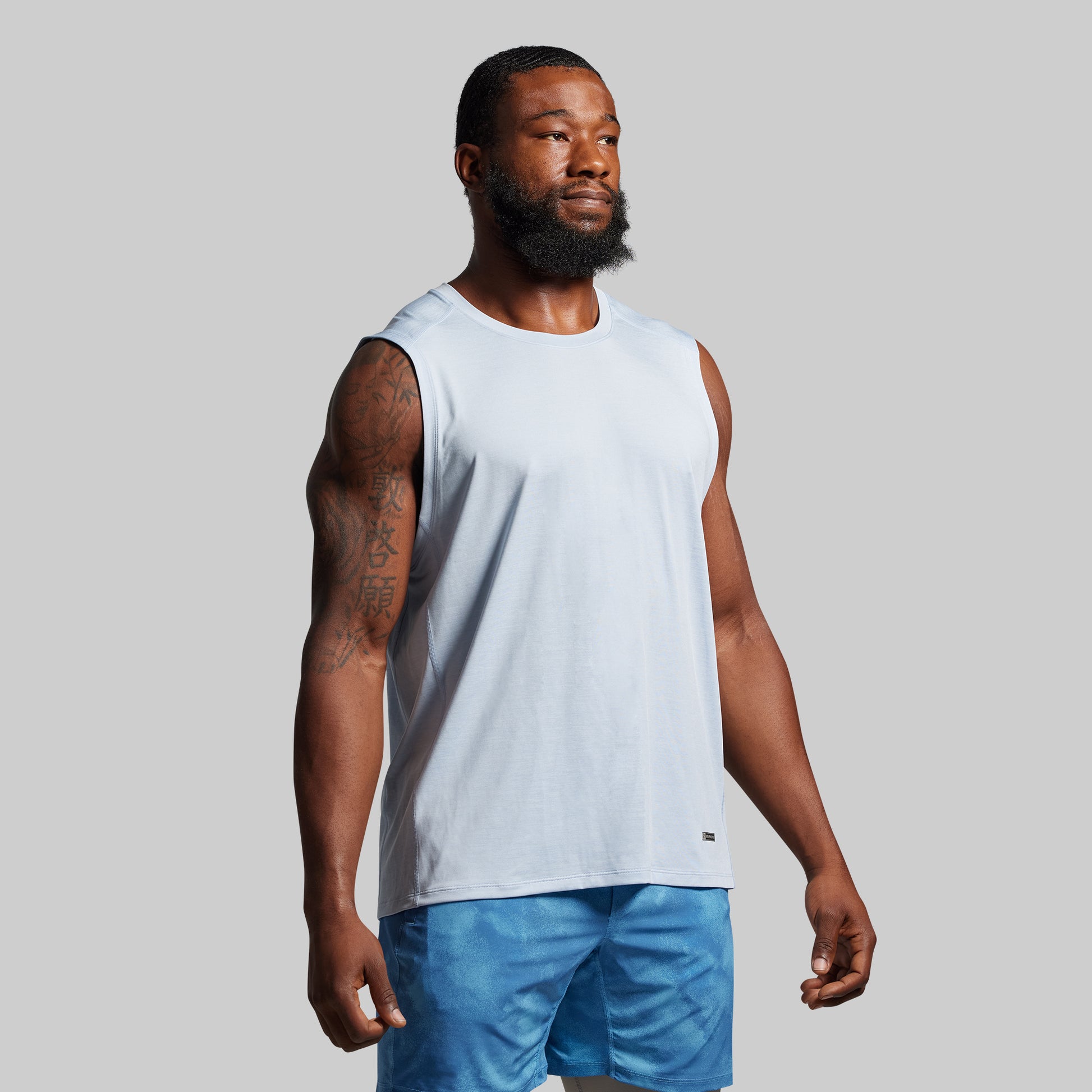 Man wearing a light blue sleeveless shirt and blue shorts on a gray background