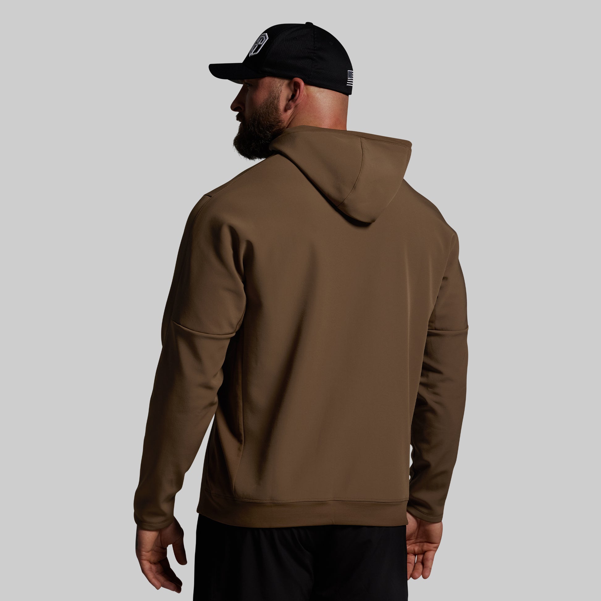 Man wearing a brown hoodie and black cap on a gray background