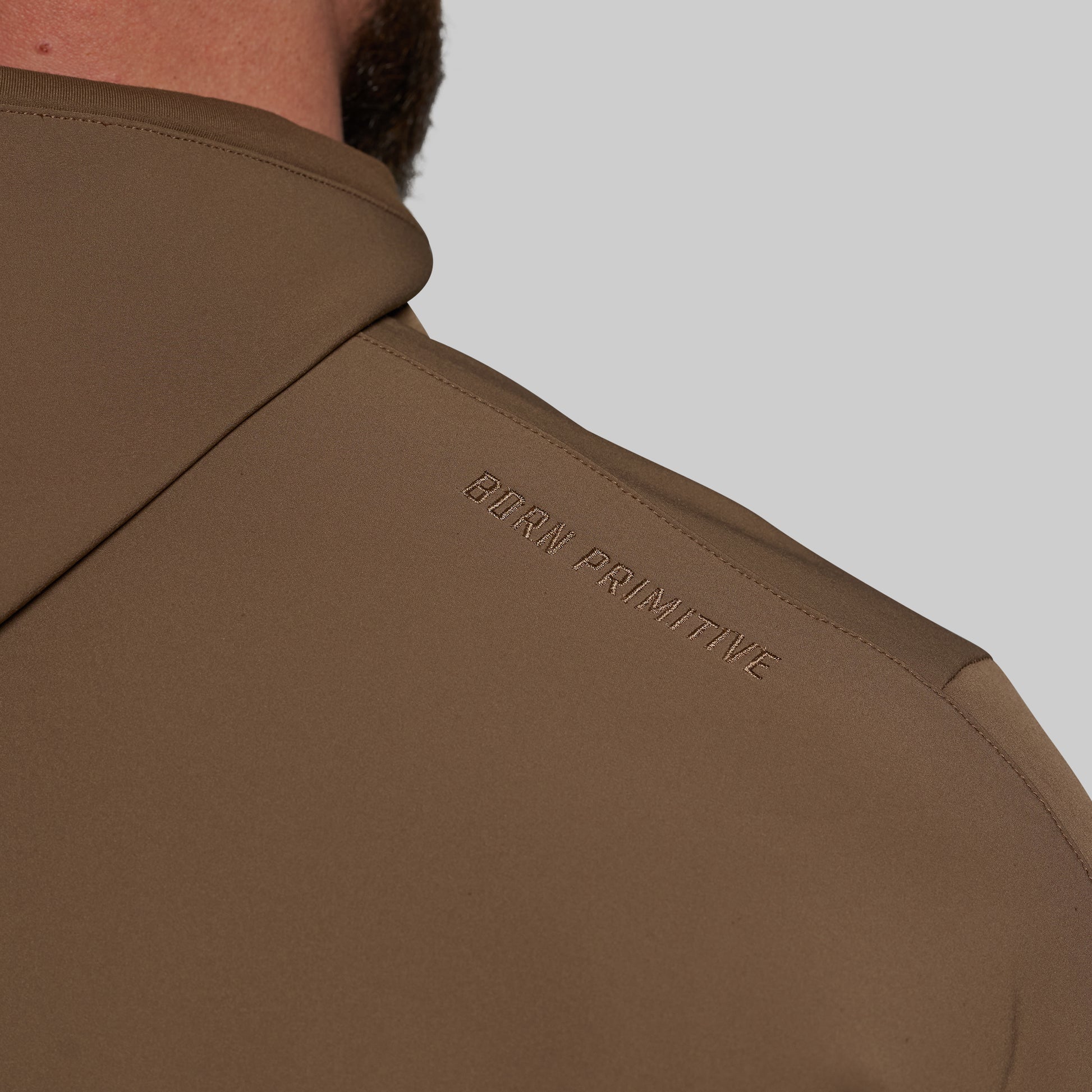 Brown jacket with 'Born Primitive' branding on a gray background