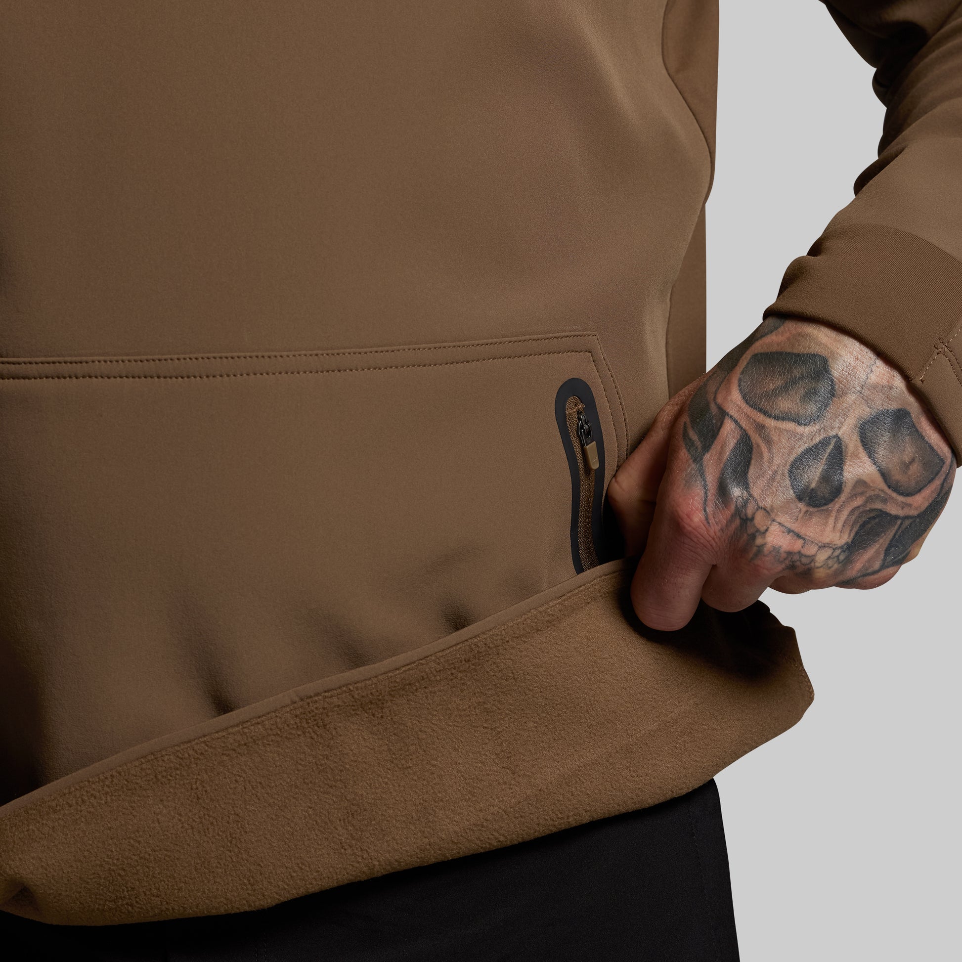Person wearing a brown jacket with a tattooed hand on a neutral background