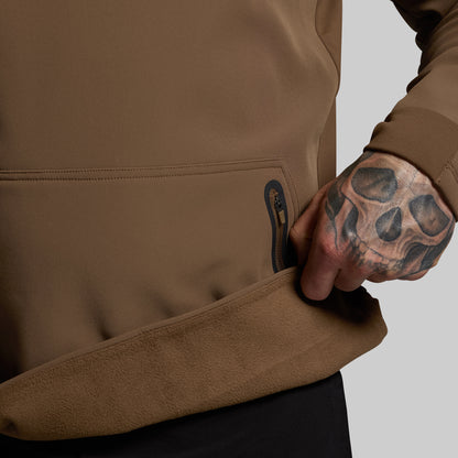 Person wearing a brown jacket with a tattooed hand on a neutral background
