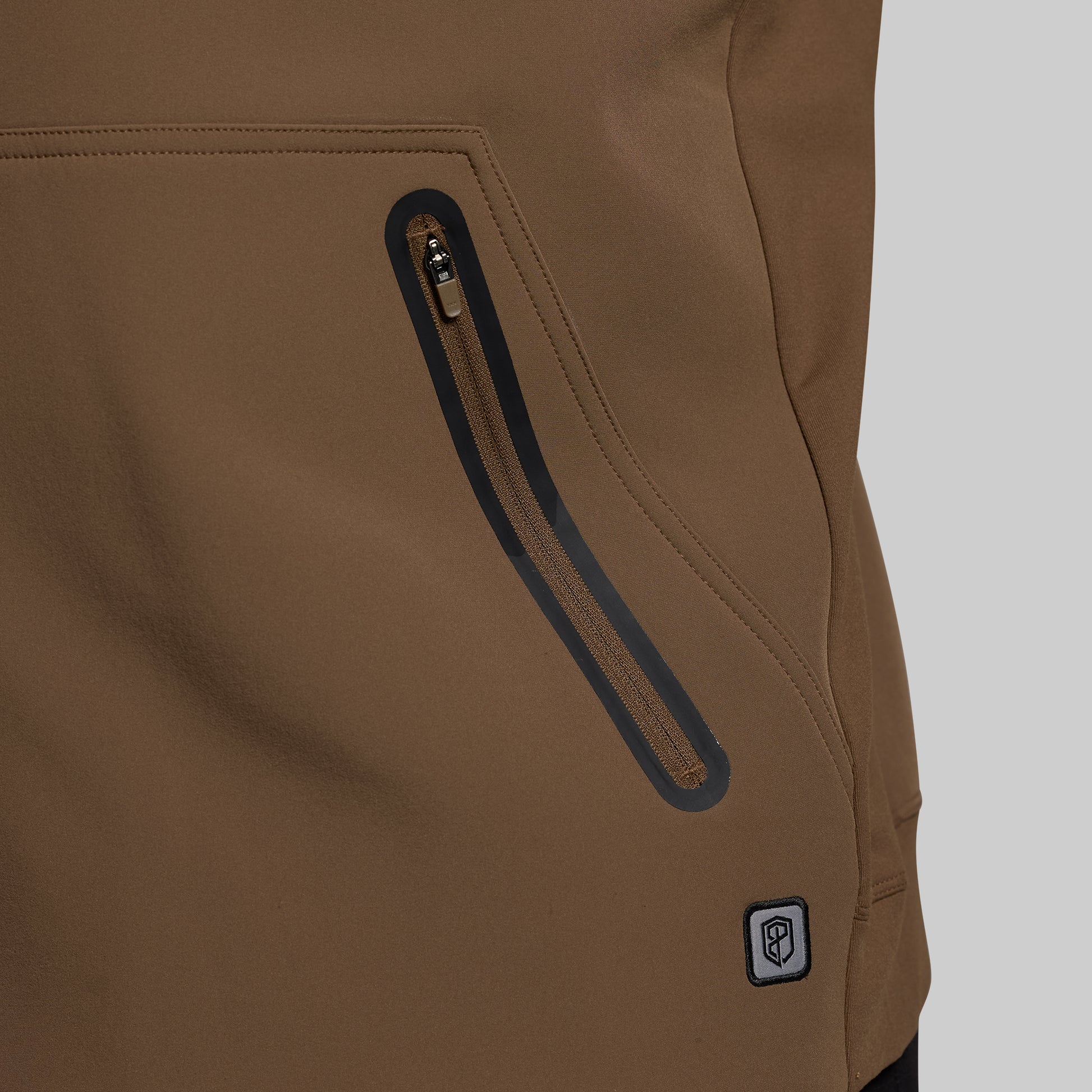 Close-up of a brown jacket with a zipper and brand logo on a gray background