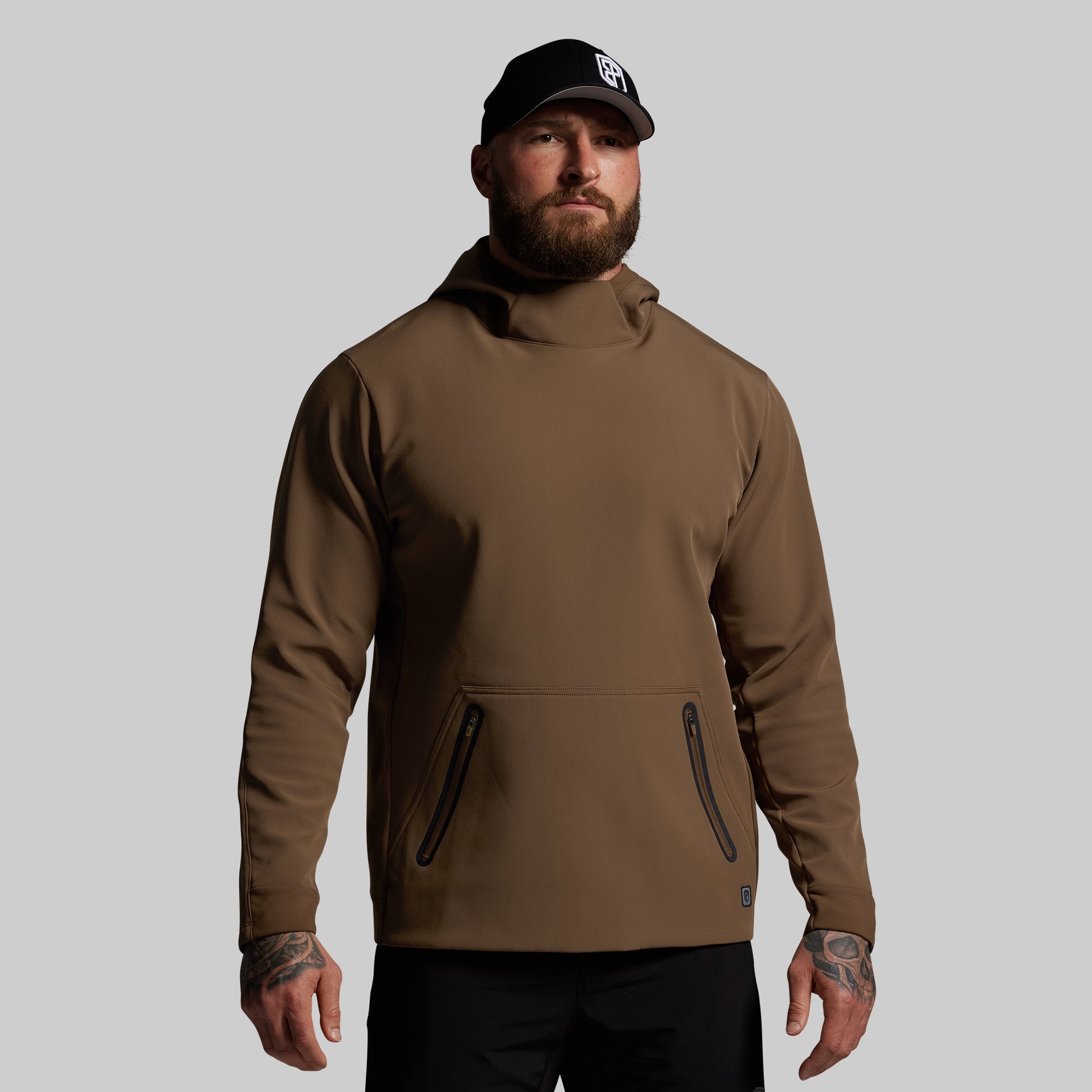 Man wearing a brown hoodie and black cap on a gray background