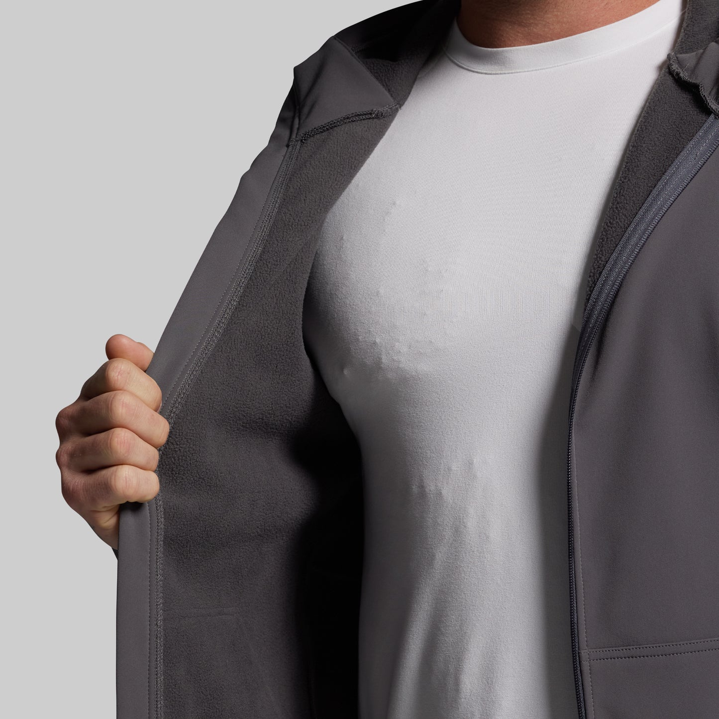 Person wearing a gray full zip hoodie over a white shirt on a light gray background