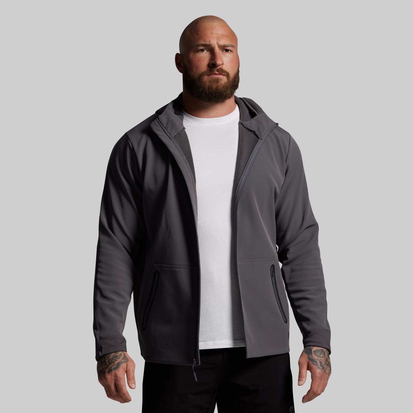 Man wearing a gray full zip hoodie over a white shirt on a gray background