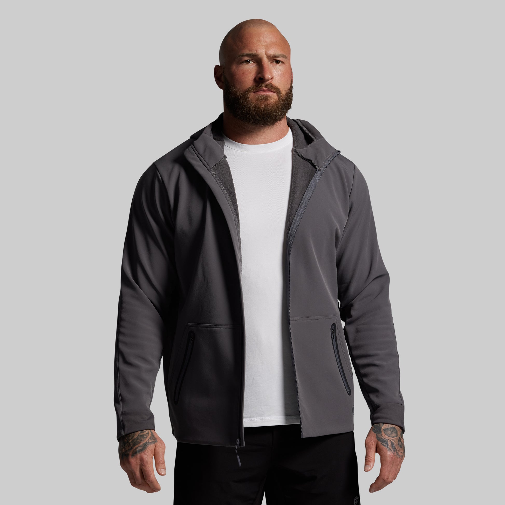 Man wearing a gray full zip hoodie over a white shirt on a gray background