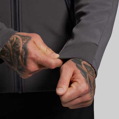 Person adjusting the cuffs of a dark gray jacket with tattooed hands.