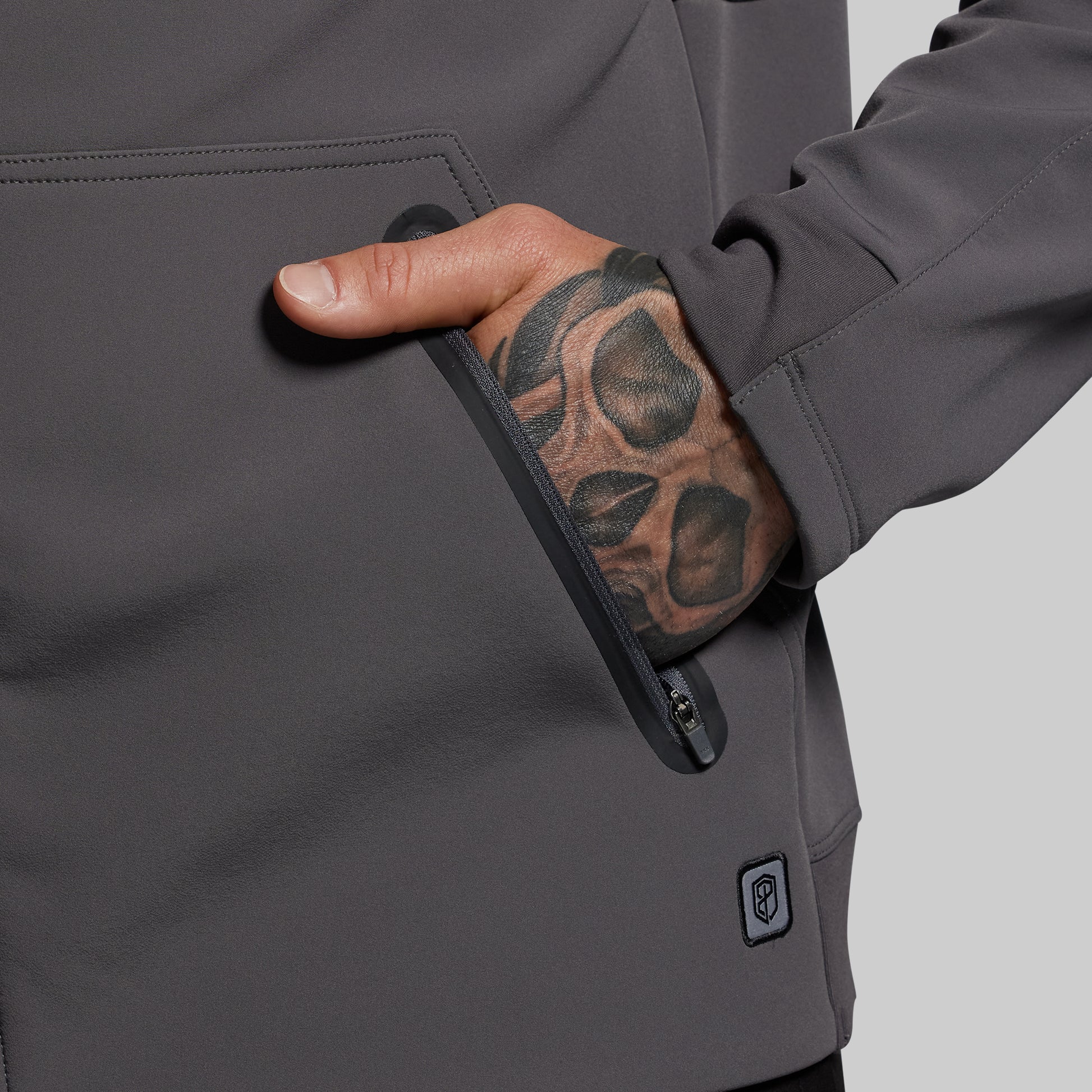 Person wearing a gray jacket with a hand in a zipper pocket, on a light gray background