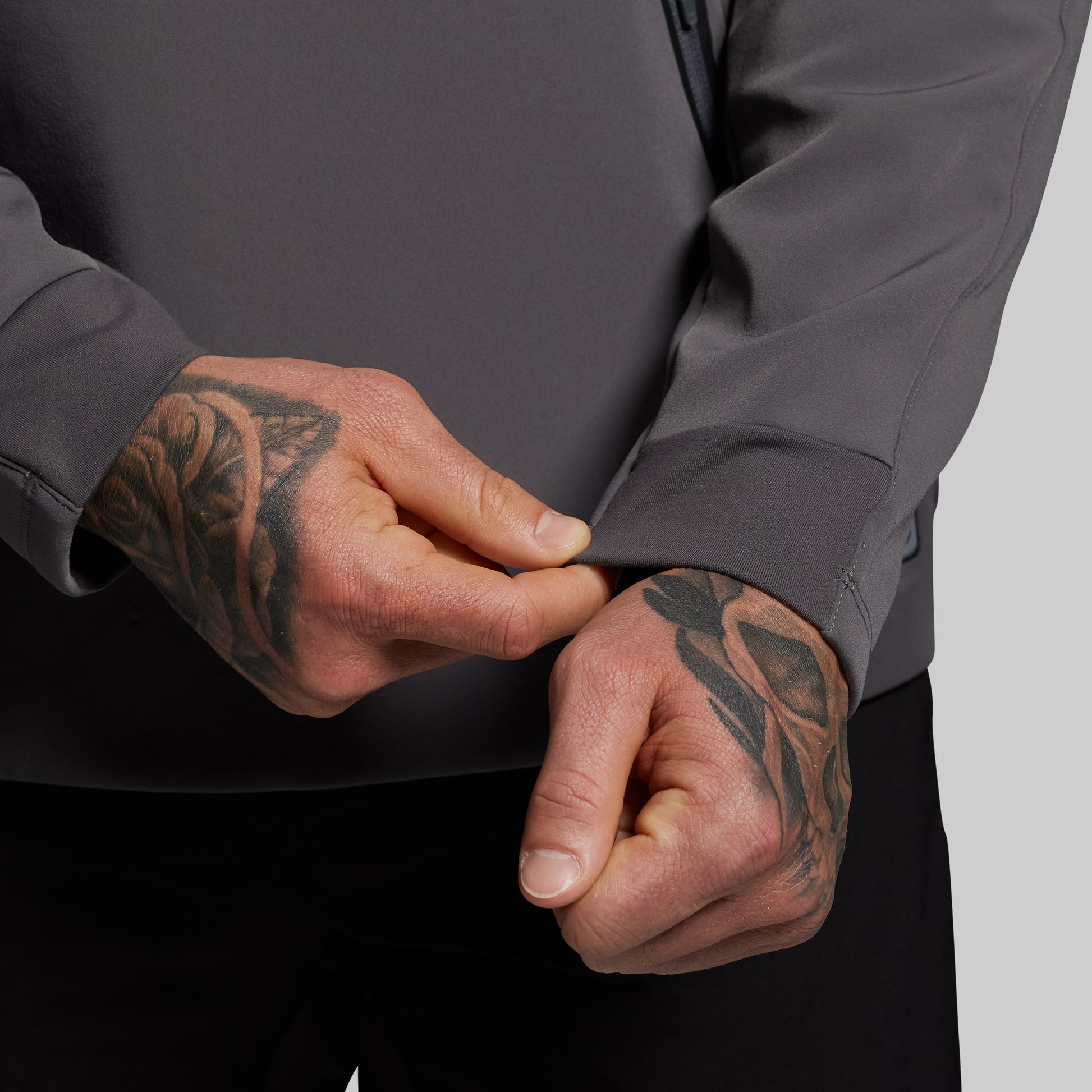 Person wearing a dark gray jacket with tattooed hands adjusting the sleeve.