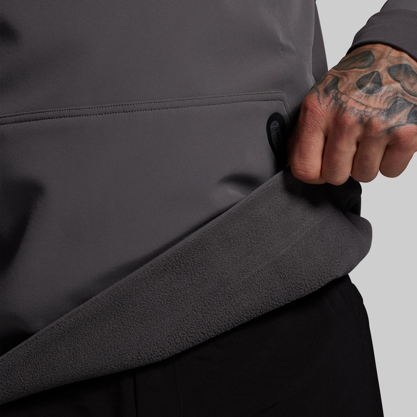 Person wearing a dark gray jacket with a tattooed arm on a light gray background