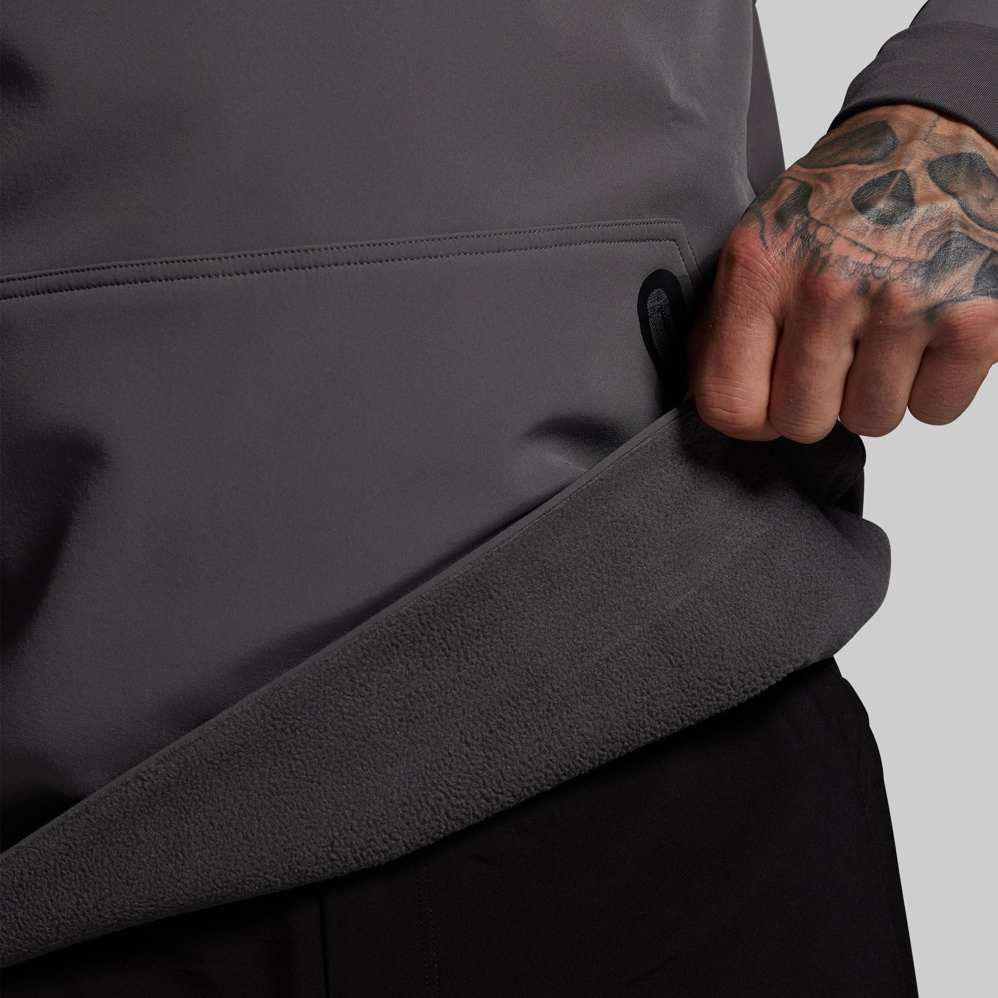 Person wearing a dark gray jacket with a tattooed arm on a light gray background