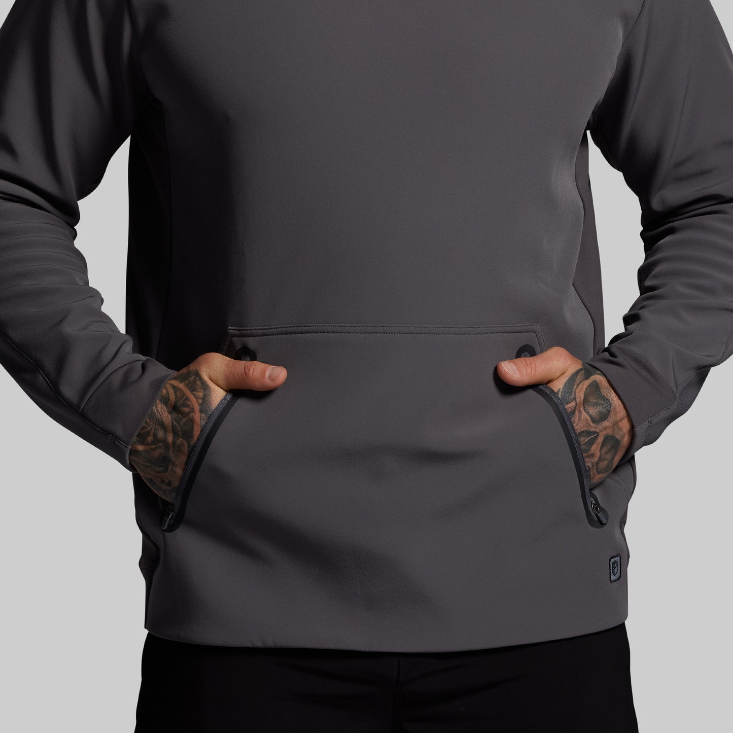 Person wearing a dark gray hoodie with tattoos on arms against a light gray background