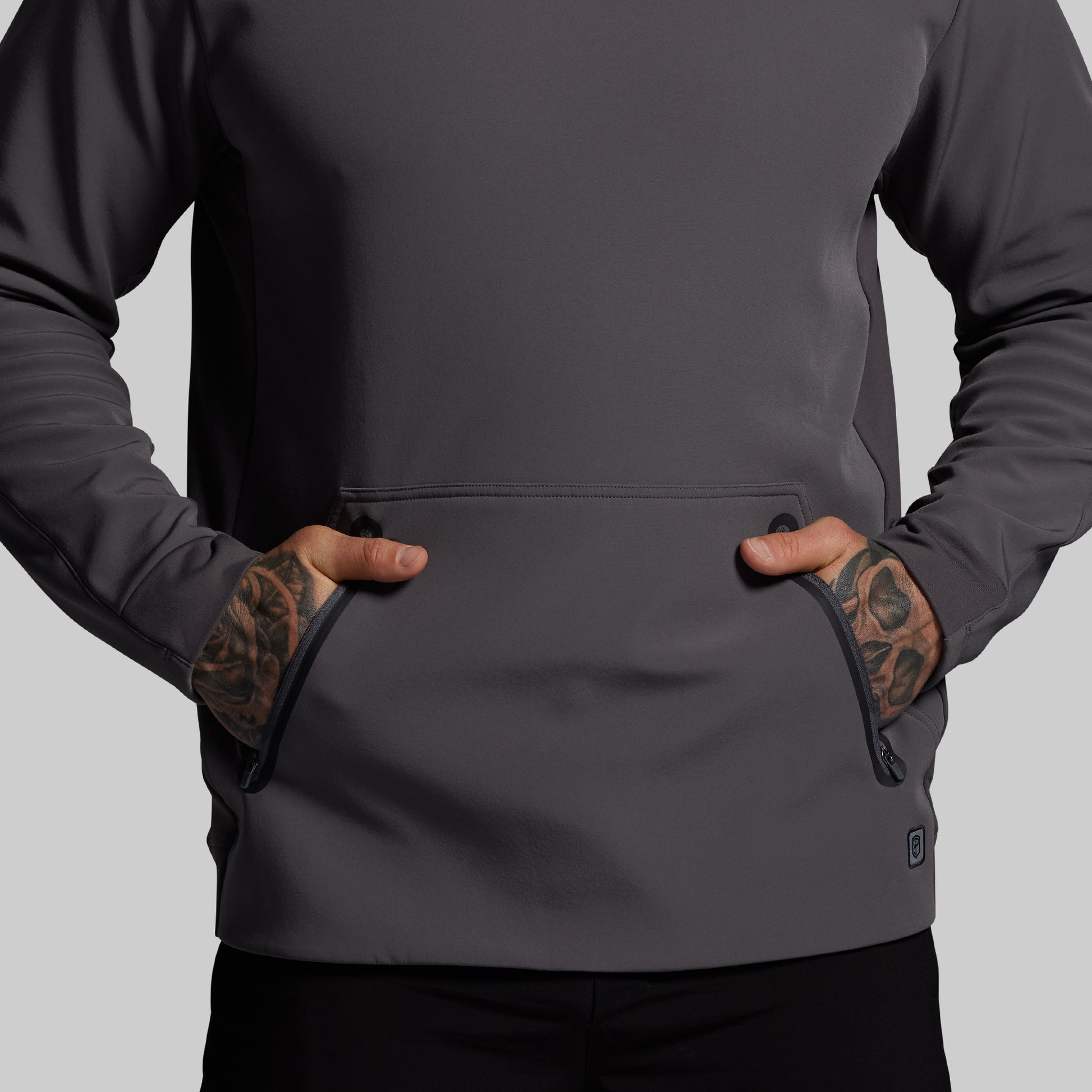 Person wearing a dark gray hoodie with tattoos on arms against a light gray background