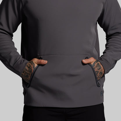 Person wearing a dark gray hoodie with tattoos on arms against a light gray background