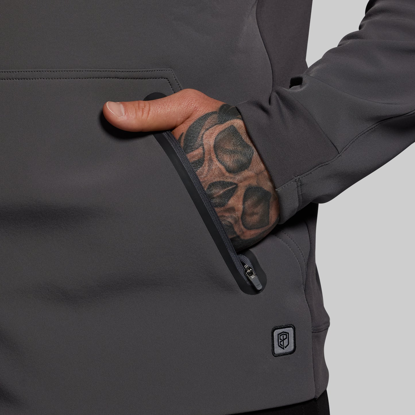 Person wearing a dark gray jacket with a visible brand logo on a light gray background