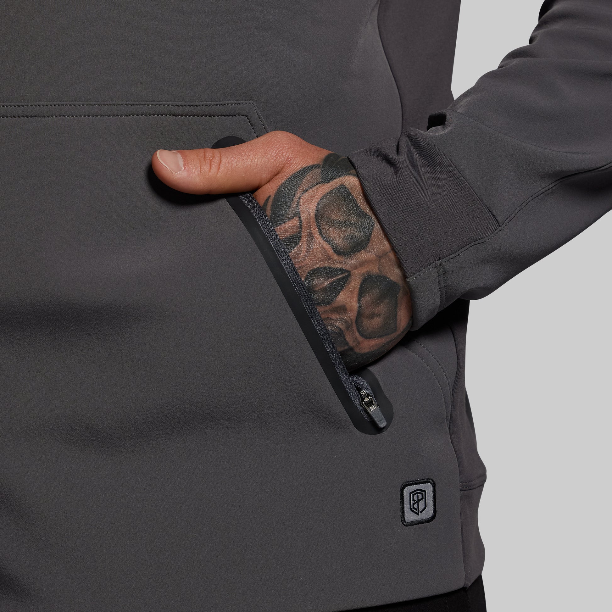 Person wearing a dark gray jacket with a visible brand logo on a light gray background