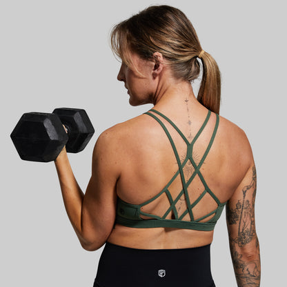 Woman lifting a dumbbell wearing a green sports bra with criss-cross straps.