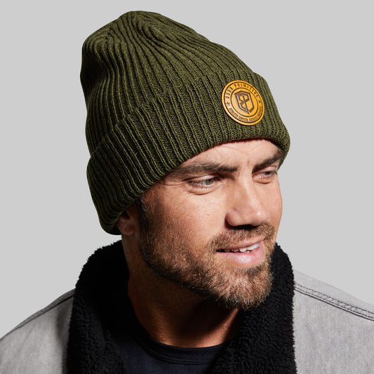 Man wearing a green beanie with a logo on a gray background