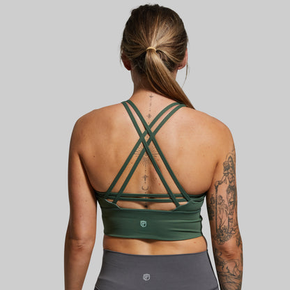 Person wearing a green sports bra and gray leggings on a plain background