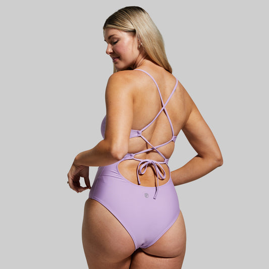 Woman wearing a purple swimsuit with criss-cross straps on a gray background